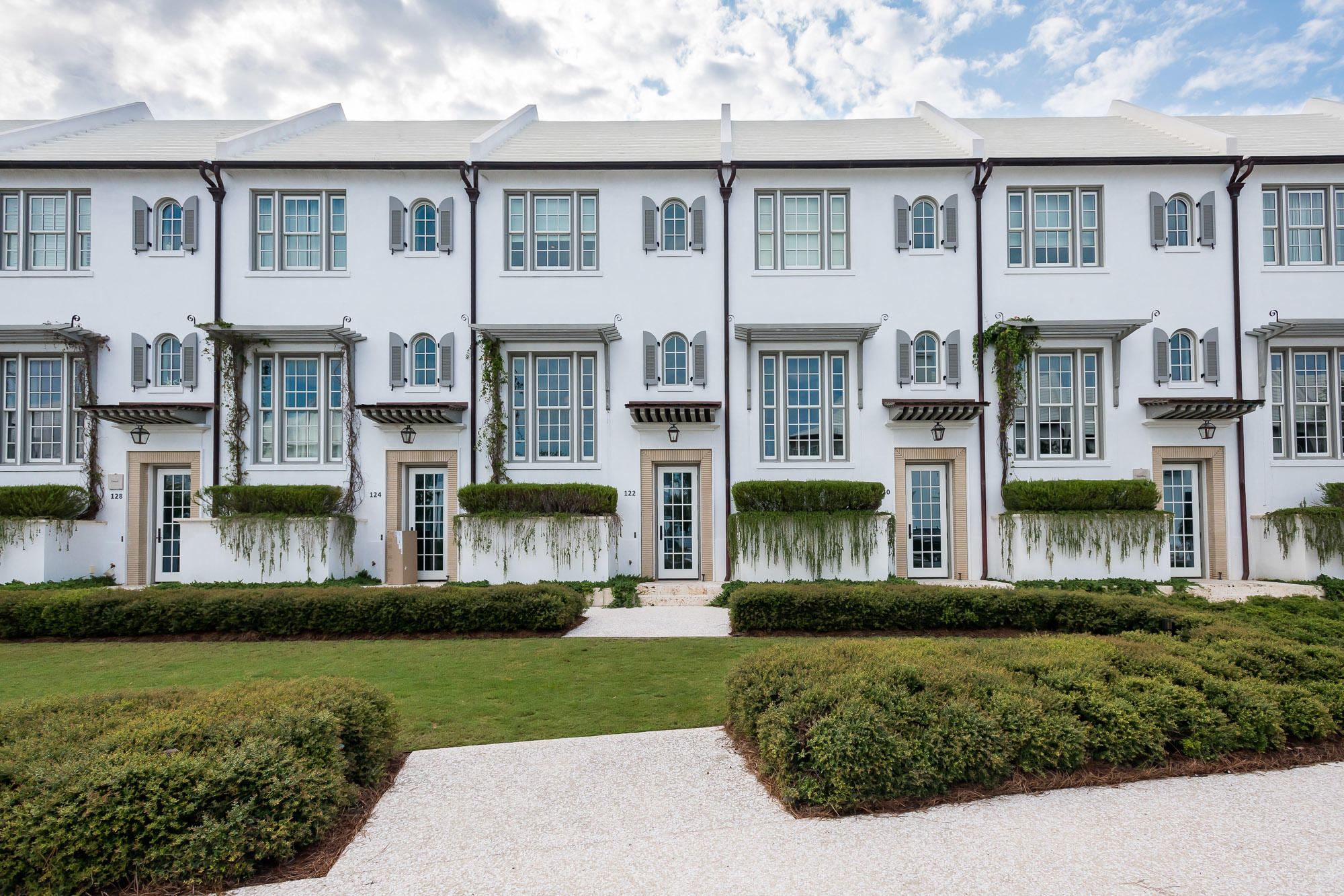 Caliza Courts residence 122, sited just south of Caliza Pool, forms a welcoming addition to Alys Beach. Designed by Khoury & Vogt Architects, the home is graced by a fronting park along N. Somerset Street, with a raised stoop entry bordered by landscaped planters. The entry and stair hall ushers one into the main living area rising one-half a floor above grade. Spanning the width of the homesite, the great room has 16-foot ceilings with 12-foot doors and windows that open to a private courtyard oasis bringing warm light into the home. Dominican Shellstone flooring carries throughout the main living levels then transitioning to the private outdoor gathering locations.  Across the courtyard is an open-air furnished loggia with upgraded SunBrite television for outdoor entertaining looking