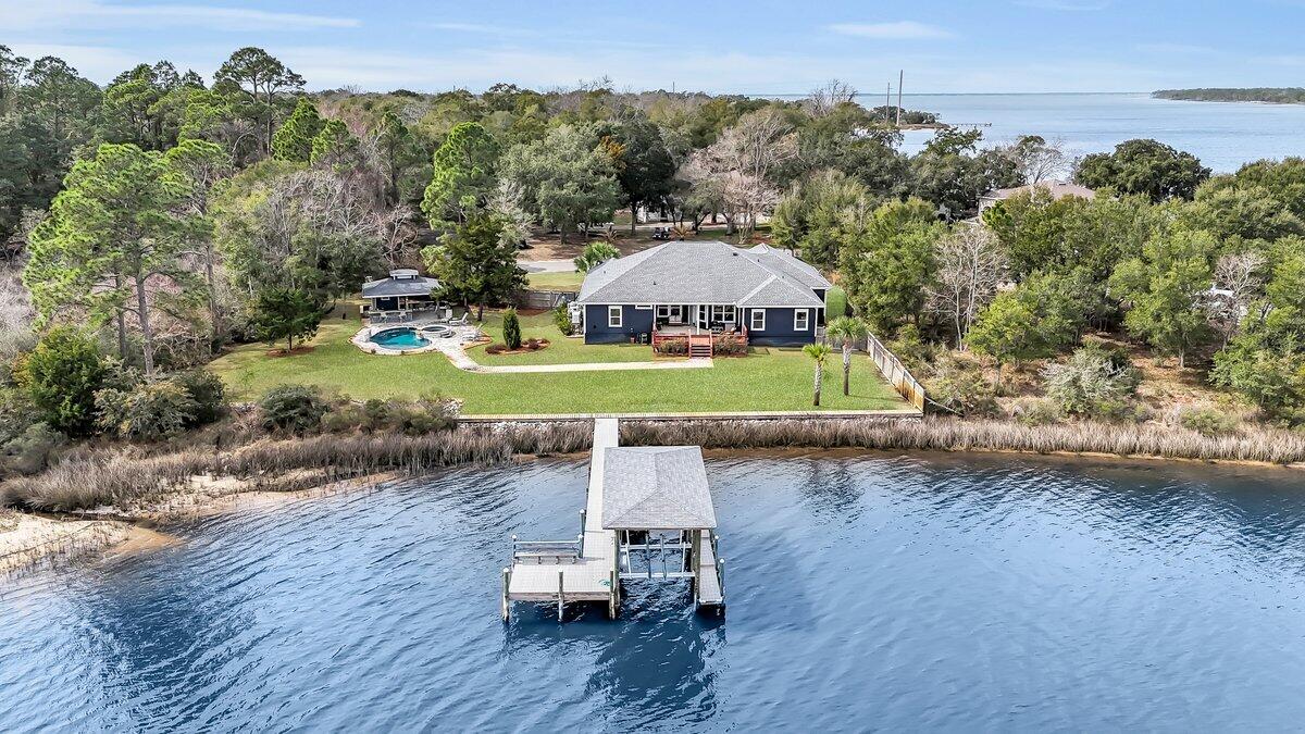Experience breathtaking waterfront living with this exceptional single-story estate situated on a rare double lot with over 200 feet of bay frontage. This stunning home boasts an open floor plan designed to maximize the panoramic water views, seamlessly blending indoor and outdoor living. Step outside to your private outdoor pool and pool house, perfect for entertaining or simply soaking in the serene coastal ambiance. Expansive windows flood the interior with natural light, offering unparalleled vistas from the living areas, kitchen, and primary suite. Wood-look tile floors create a warm and inviting atmosphere while offering durability and easy maintenance. Barnwood accents add a touch of rustic elegance, enhancing the coastal charm of the space. The kitchen breakfast area overlooks the The kitchen and bathrooms showcase crisp white cabinetry paired with gorgeous white quartz countertops, creating a bright, airy, and timeless aesthetic. The kitchen breakfast area overlooks the bay and a separate dining room provides extra entertaining space. The primary bedroom boasts a large walk in closet and spacious bath, including a nice tiled shower and a soaking tub. One guest room overlooks the bay and has a private bath. The other two guest rooms share a hall bath. There is plenty of garage parking and storage in the 3 car garage. Park your boat at the dock, complete with lift, for convenient 1qweaesaaaaaaaaaaabeautiful sunset rides. This unique property is a rare opportunity to own a spacious waterfront retreat with ample outdoor space, stunning sunsets, and direct access to the bay. Don't miss your chance to own this one-of-a-kind coastal gem!