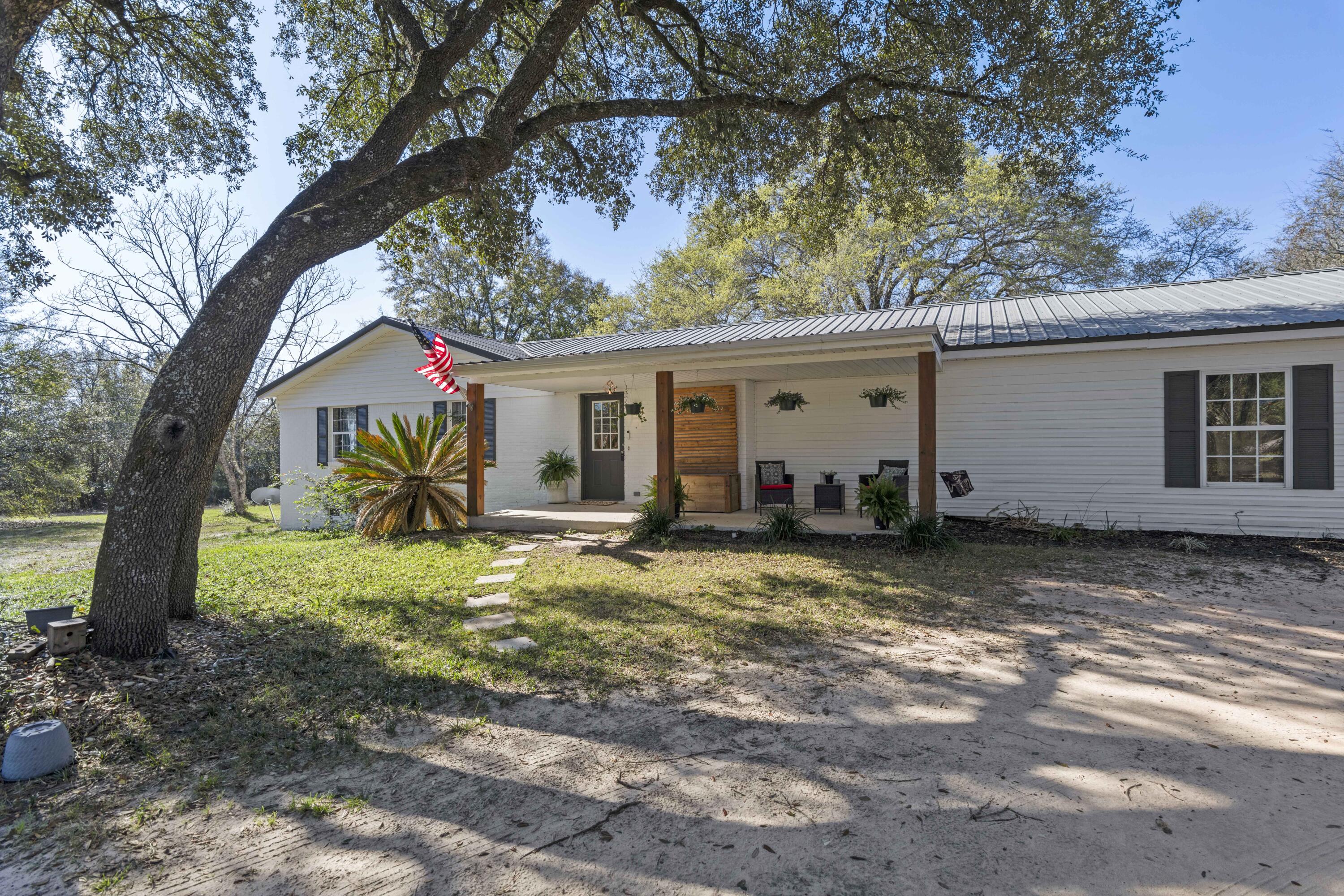 Drive up your private driveway, lined with mature azalea bushes, to your peaceful 4+ acre homestead. This beautifully renovated 4-bedroom home features a split floor plan, with the fourth bedroom offering privacy for a mother-in-law suite. Two spacious living areas, an open kitchen, and a bright Florida room provide plenty of space to relax and entertain while overlooking lush blueberry bushes and walnut trees. The property includes a large barn wired with electricity and a 4 space carport. Located just 35 minutes from Eglin AFB and 20 minutes from 7th Group, this home offers the perfect blend of country charm and modern convenience!