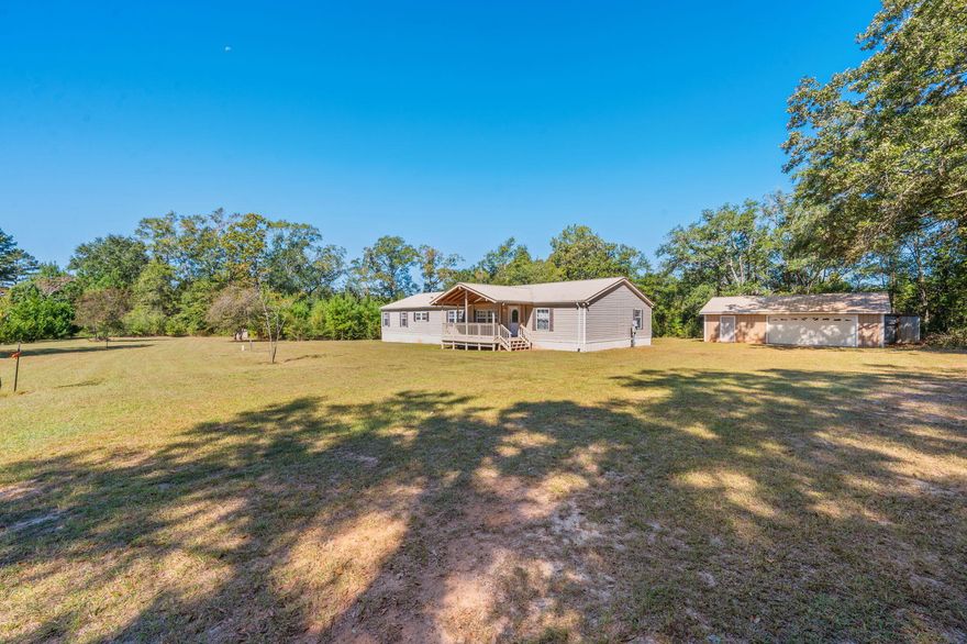 Looking for room to roam and relax? This beauty sits proudly on 2 acres and welcomes you in with a large covered front porch perfect for morning coffee or evening unwinds. Step inside to over 2,300 sq ft of living space with an open concept layout featuring a cozy wood burning fireplace, dining area, bonus room, and a kitchen that'll make any home chef swoon. Complete with a massive island and all appliances included! Faux stone accents add rustic charm throughout. With 4 bedrooms and 2 full bathrooms, there's space for everyone. The ensuite is your personal retreat with a double vanity, separate shower, large soaking tub, and a roomy walk-in closet. Vinyl flooring and soft carpet flow throughout the home. Out back, a spacious covered deck with ceiling fans sets the stage for grillin' and chillin'. Just steps away, you'll find a detached 2-car garage with workshop and an extra yard building for storage. With a durable metal roof and easy care vinyl siding, this one's got the looks and the longevity. Your country comfort dream home is calling so you better answer!