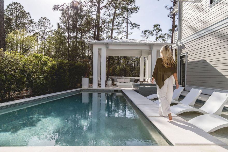 In WaterColor, the most compelling homes rarely announce themselves. They reveal their intention gradually, through proportion, material, and the quiet confidence of thoughtful design. At 565 East Royal Fern, that restraint is immediately evident. Built by Borges Brooks Builders and designed by TS Adams, the residence reads less like a vacation home and more like a carefully composed coastal compound, where architecture, craftsmanship, and livability were considered in equal measure.

The interiors are grounded in warmth and texture. Oak floors by Seashore Flooring run throughout, softening the scale of the home while complementing a restrained palette of whites and natural woods. Light moves easily across the living spaces, filtered through expansive openings and framed by subtle architectural details. Several furnishings were custom designed by the homeowner and executed by Amish craftsmen, introducing a quiet layer of authenticity that reinforces the home's tailored, intentional feel.

The kitchen is both sculptural and functional, centered around a waterfall island that anchors the space. Dome pendants add a clean architectural focal point, while a 60-inch Wolf range and Liebherr refrigerator elevate the appliance package without disrupting the home's understated tone. In the carriage house, quartz countertops and coordinated finishes continue the same level of detail, ensuring the secondary living spaces feel fully integrated with the main residence.

With eight bedrooms, including the private carriage house, the property lives as a true compound. The primary suite is positioned as a retreat, complete with a spa-style bathroom featuring a soaking tub, electric fireplace, dual closets, and direct access to a private patio. Guest accommodations are thoughtfully distributed, allowing for both privacy and flexibility when hosting extended family and visitors.

Construction details further distinguish the home. The slab is elevated and foam insulated, a deliberate structural decision that enhances stability and helps prevent floor movement over time. Real stone in the downstairs guest bathroom reinforces the emphasis on authentic materials, while EPAY decking across the outdoor living areas was selected for long-term durability in the coastal environment.

Outdoor spaces extend the architecture rather than compete with it. A resort-style pool and covered pavilion create layered gathering areas, allowing the home to transition naturally between quiet mornings and larger-scale entertaining.

At 565 East Royal Fern, the result is not simply scale, but composition. A WaterColor residence defined by intention, craftsmanship, and a quieter, more enduring interpretation of coastal luxury.