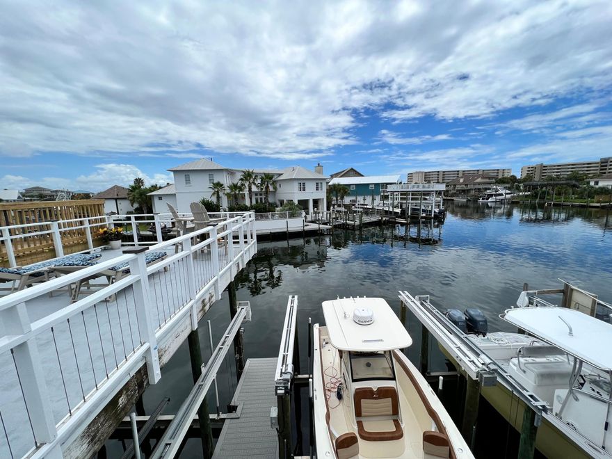 Along the protected canals of Destin Harbor, this fully renovated waterfront townhome captures the essence of elevated coastal living with the rare advantage of a deeded 40-foot boat slip complete with a lift. Set on Holiday Isle, moments from private beach access, the residence pairs boating convenience with refined interiors designed for effortless days on the water. Spanning 1,576 square feet across two thoughtfully designed levels, this three-bedroom, three-bath custom townhouse has been meticulously updated from top to bottom. The main living area welcomes with vaulted ceilings and exposed beam detailing, creating an airy architectural statement that frames the open-concept design. Hardwood and tile flooring run throughout, complemented by curated coastal décor and custom furnishings that convey polish without pretense. The renovated kitchen is both stylish and functional, outfitted with stainless steel appliances, ample cabinetry, a generous breakfast bar, and modern lighting that enhances the clean lines of the space. It flows seamlessly into the dining and living areas, making everyday living and entertaining feel equally inviting. Outdoor living unfolds on two distinct levels. At water level, a covered patio offers a shaded retreat just steps from your private slip, ideal for morning coffee before a cruise through the harbor. Above, an expansive upper deck with a built-in grill station creates a natural gathering place for sunset dinners and relaxed evenings carried by harbor breezes. The first-floor primary suite serves as a tranquil escape with direct access to the outdoor living space. A custom closet system maximizes organization, while the beautifully updated bath features a soaking tub, glass-enclosed shower, and designer tile work that lends a spa-inspired feel. A split-bedroom floor plan ensures privacy for family and guests, with two additional bedrooms and two full baths offering comfort and flexibility. With direct water access, a deeded boat slip, refined finishes, and proximity to Holiday Isle beach access, this turnkey residence presents an exceptional opportunity for full-time waterfront living or a sophisticated harbor retreat designed around life on the water.