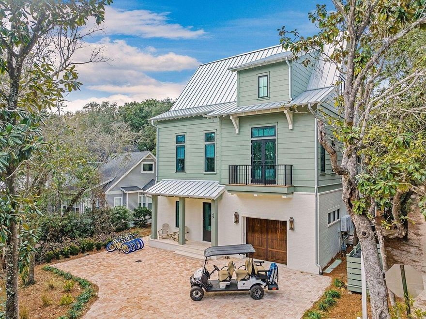 Defined by a clean coastal exterior of white brick, Hardie plank siding, and a metal roof, 69 Live Oak Street presents a timeless architectural profile across four thoughtfully designed levels, the result of a collaboration between architects Leslie Schwartz and Rob Bounds of 30A North Design and builder Timothy O'Hara of Coastal Custom Builders. Seamlessly set among the old growth oaks of Old Seagrove, and ideally positioned just 200 yards from the Live Oak Street beach access, the home offers convenient proximity to the Gulf while maintaining a sense of privacy. A dedicated game room anchors the ground floor, where soaring 12-foot shiplap ceilings frame a relaxed gathering space with multiple seating areas, shuffleboard, and pinball. Just beyond, the outdoor living area extends the experience with a private pool, spa, and fully equipped summer kitchen--designed for seamless indoor-outdoor entertaining. Two king guest suites offer privacy and comfort, setting the tone for the home's ability to comfortably accommodate guests from the moment you enter. A full laundry room with dual washers and dryers, owner's storage, mudroom, and garage access complete the level, all connected by elevator service to the upper floors.
The main living level unfolds with an open layout designed for hosting at scale. A spacious den and secondary sitting area flow into a dining space that comfortably accommodates large gatherings, all centered around a chef's kitchen featuring a 6-by-12-foot quartz island, an eight-burner Wolf range, and integrated Sub-Zero refrigeration. A secondary prep area provides additional workspace and storage, supporting effortless entertaining. This level also includes a private king suite and a bunk room with custom queen-over-queen accommodations, further expanding the home's flexible sleeping capacity.

Upstairs, the primary suite offers a quiet retreat, complete with a spa-like bath featuring dual vanities, a soaking tub, and a separate shower, along with direct access to a private balcony overlooking the backyard. Additional king guest suites and multiple bunk configurations create a layout designed to comfortably host large groups while maintaining a sense of privacy throughout.
The fourth level is dedicated entirely to an open-air rooftop deck, where treetop views of Old Seagrove and expansive skies create a setting equally suited for morning coffee or evening gatherings.
Designed with both lifestyle and performance in mind, the home accommodates up to 28 guests and presents an opportunity meaningful annual rental income.