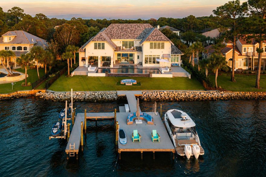 Rare Bayfront Opportunity. Constructed with concrete and just 3 years young, this showpiece pairs resort-style amenities with a technology-forward, luxury interior and 112 feet of prime waterfront. Enjoy 7,020 sq ft of finished, heated/cooled space now, with an additional 2,955 sq ft pre-wired and plumbed for your ideal use and design.
Inside, it's all about scale, light, and livability. Twelve-foot ceilings, 4'x2' tile throughout, double staircases crowned by chandeliers, and three sets of 9' sliding glass doors framing the bay. A chef's kitchen that actually cooks features Wolf and Electrolux Commercial appliances and touchless faucets. Entertain guests in your climate-controlled, glass-enclosed wine cellar capable of holding more than 1,000 bottles of wine. The primary suite brings hotel-level luxury with dual oversized closets and a 13'x7' spa shower (multiple shower heads, integrated speakers) and a free-standing tub. 
An oversized, storage-rich laundry room keeps life tidy. Whole-home conveniences include a central vacuum, security system with fire monitoring, full CCTV with motion detection, and a hidden concrete safe room with its own monitoring. Outdoor living is the headliner. A 1,435 sq ft 4-car garage anchors the motor court, while the covered summer kitchen brings the party: 42" commercial grill, commercial double burner, 60" Wolf hood with dual external vents, outdoor pizza oven (not built-in), 62" Arctic Air under-counter commercial refrigerator, NatureKast cabinetry, touchless faucet, wall-mounted Lava Aire fan/mister, Big Ass Fan, Hishizaki icemaker, and a 9'x4' island. Three remote screen enclosures open to a 50'x20' saltwater, ozone-filtered pool with water features, a 13'x16' spa with swim-in-place jet, commercial gas heater, two chillers, five in-pool barstools facing the bay, LED lighting, ten gas lanterns, a built-in fire pit, lounge seating (6 patio loungers + 2 pool loungers), two 70" outdoor TVs, Bose + Sonos audio, and a large storage room.
Your private waterfront playground. An oversized dock built with flow-through decking is specked for a future boat lift and includes a kayak deck, two 360-degree jet ski lifts, three ladder access points, perimeter uplighting, and full utilities--power, water, internet, and cameras--right on the dock. For added peace of mind, this home also features exterior perimeter security cameras, alarm system with fire monitoring, a solid concrete hidden safe room with CCTV camera systems, a cell tower, and a 48 KW Generac generator.