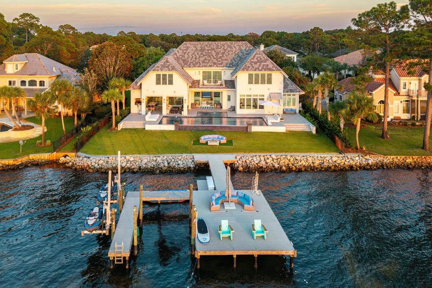 Rare Bayfront Opportunity. Constructed with concrete and just 3 years young, this showpiece pairs resort-style amenities with a technology-forward, luxury interior and 112 feet of prime waterfront. Enjoy 7,020 sq ft of finished, heated/cooled space now, with an additional 2,955 sq ft pre-wired and plumbed for your ideal use and design.
Inside, it's all about scale, light, and livability. Twelve-foot ceilings, 4'x2' tile throughout, double staircases crowned by chandeliers, and three sets of 9' sliding glass doors framing the bay. A chef's kitchen that actually cooks features Wolf and Electrolux Commercial appliances and touchless faucets. Entertain guests in your climate-controlled, glass-enclosed wine cellar capable of holding more than 1,000 bottles of wine. The primary suite brings hotel-level luxury with dual oversized closets and a 13'x7' spa shower (multiple shower heads, integrated speakers) and a free-standing tub. 
An oversized, storage-rich laundry room keeps life tidy. Whole-home conveniences include a central vacuum, security system with fire monitoring, full CCTV with motion detection, and a hidden concrete safe room with its own monitoring. Outdoor living is the headliner. A 1,435 sq ft 4-car garage anchors the motor court, while the covered summer kitchen brings the party: 42" commercial grill, commercial double burner, 60" Wolf hood with dual external vents, outdoor pizza oven (not built-in), 62" Arctic Air under-counter commercial refrigerator, NatureKast cabinetry, touchless faucet, wall-mounted Lava Aire fan/mister, Big Ass Fan, Hishizaki icemaker, and a 9'x4' island. Three remote screen enclosures open to a 50'x20' saltwater, ozone-filtered pool with water features, a 13'x16' spa with swim-in-place jet, commercial gas heater, two chillers, five in-pool barstools facing the bay, LED lighting, ten gas lanterns, a built-in fire pit, lounge seating (6 patio loungers + 2 pool loungers), two 70" outdoor TVs, Bose + Sonos audio, and a large storage room.
Your private waterfront playground. An oversized dock built with flow-through decking is specked for a future boat lift and includes a kayak deck, two 360-degree jet ski lifts, three ladder access points, perimeter uplighting, and full utilities--power, water, internet, and cameras--right on the dock. For added peace of mind, this home also features exterior perimeter security cameras, alarm system with fire monitoring, a solid concrete hidden safe room with CCTV camera systems, a cell tower, and a 48 KW Generac generator.