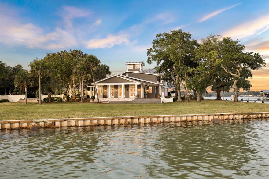 Few properties on Florida's Emerald Coast can claim what 11 Paradise Point Road delivers: a private covered boathouse with a full boat slip, over an acre of waterfront land, and direct access to Choctawhatchee Bay. Set at the corner where Garnier Bayou meets Poquito Bayou in historic Shalimar, this is the kind of lot that simply does not come available. Water on two sides, a seawall running the full length of the property, and a manicured lawn sweeping to the shoreline beneath a canopy of generational live oaks. The boathouse is deep, protected, and ready for daily use, whether that means a morning run to Destin Harbor, an afternoon on the open bay, an evening on the sandbar, or simply fishing off the dock at golden hour. For those who live on the water, this property was built for it.
 
The setting carries history as well as beauty. Shalimar was named for the legendary Mughal gardens of Kashmir, a place synonymous with paradise and natural beauty, and this small, storied town has quietly anchored life along the bayou for over a century. Streets shaded by ancient live oaks, shores shaped by the gentle tides of the bayou, and a character that has endured while the rest of the Emerald Coast grew up around it.

The estate spans 6,591 square feet across three thoughtfully designed stories. A circular paver driveway winds through mature oaks and palms to a stately coastal Southern facade: grey board-and-batten siding, a standing seam metal roof, soaring white columns, and a covered wraparound porch finished in stone tile with open water views. Inside, a grand great room anchors the main level, with walls of French doors opening to the waterfront porch. Hardwood floors, beadboard ceilings, and crown molding carry throughout. The kitchen features granite countertops, warm wood cabinetry, and stainless appliances. A billiard room, formal dining space, and full laundry room complete the level. The primary suite offers direct bayou views, a soaking tub, and a walk-in shower. A sweeping second-floor balcony delivers panoramic views of both bayous. The third floor houses a private observatory above the treeline. Two gas fireplaces, multiple patio areas, a firepit, and attached garage complete this exceptional offering, all within close proximity to Destin and Fort Walton Beach.