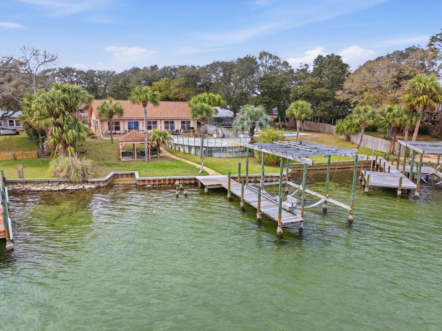 Positioned on Â½ acre along the tranquil waters of Cinco Bayou, this exceptional waterfront estate at 144 Monahan Drive offers a rare blend of privacy, craftsmanship, and coastal lifestyle living. Designed for both comfort and entertainment, the property combines timeless finishes with distinctive architectural details throughout. Inside, expansive living areas showcase vaulted ceilings, cedar accent walls, built-in bookcases, and fireplace that create warmth and character. Travertine, porcelain tile, bamboo, Brazilian cherry, cork, and wood-style plank flooring reflect the custom quality found in every space. The chef's kitchen is appointed with built-in appliances and travertine flooring, flowing seamlessly into generous dining and gathering areas ideal for hosting. The waterfront primary suite offers serene views and a spa-inspired bath featuring a soaking tub, bidet, oversized tiled shower, and custom walk-in closet. A private apartment lockout with skylights and bay window provides flexible accommodation for guests or multigenerational living. Outdoors, resort-style living awaits with a kidney-shaped in-ground pool, expansive paver deck, gazebo, and large wooden waterfront deck. Boating enthusiasts will appreciate the dock and lift (conveyed as-is), offering direct access to the bayou lifestyle. Additional highlights include a 12-12.5KW generator supporting major systems, whole-house water softener, detached 40x10 powered workshop, detached two-car garage, carport, and circular drive. This is more than a waterfront home it is a private coastal retreat in the heart of Fort Walton Beach, offering space, flexibility, and unforgettable sunsets over Cinco Bayou.