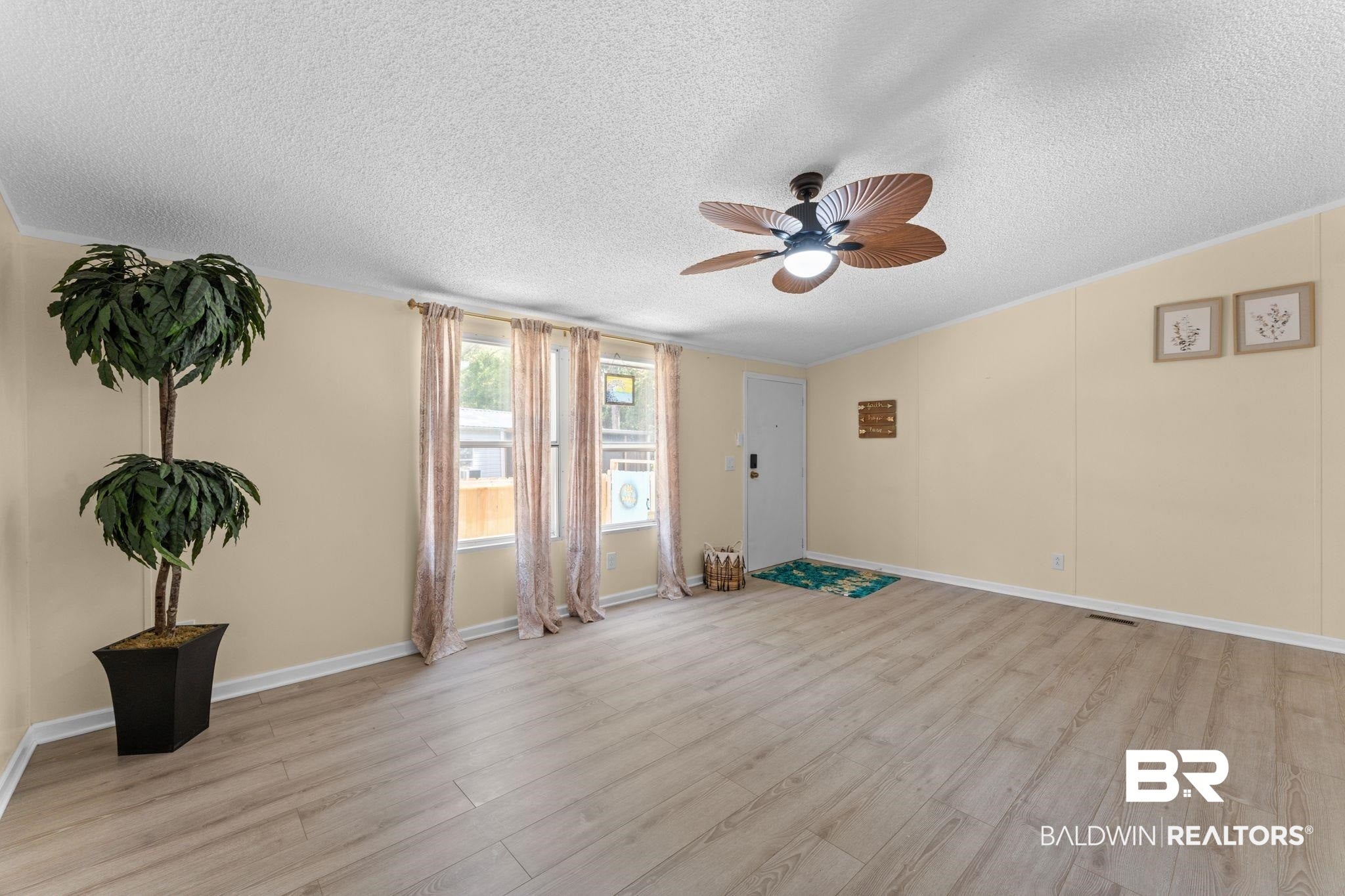 Spacious living area featuring light wood-finish flooring, multiple windows providing natural illumination, and a ceiling fan with integrated lighting