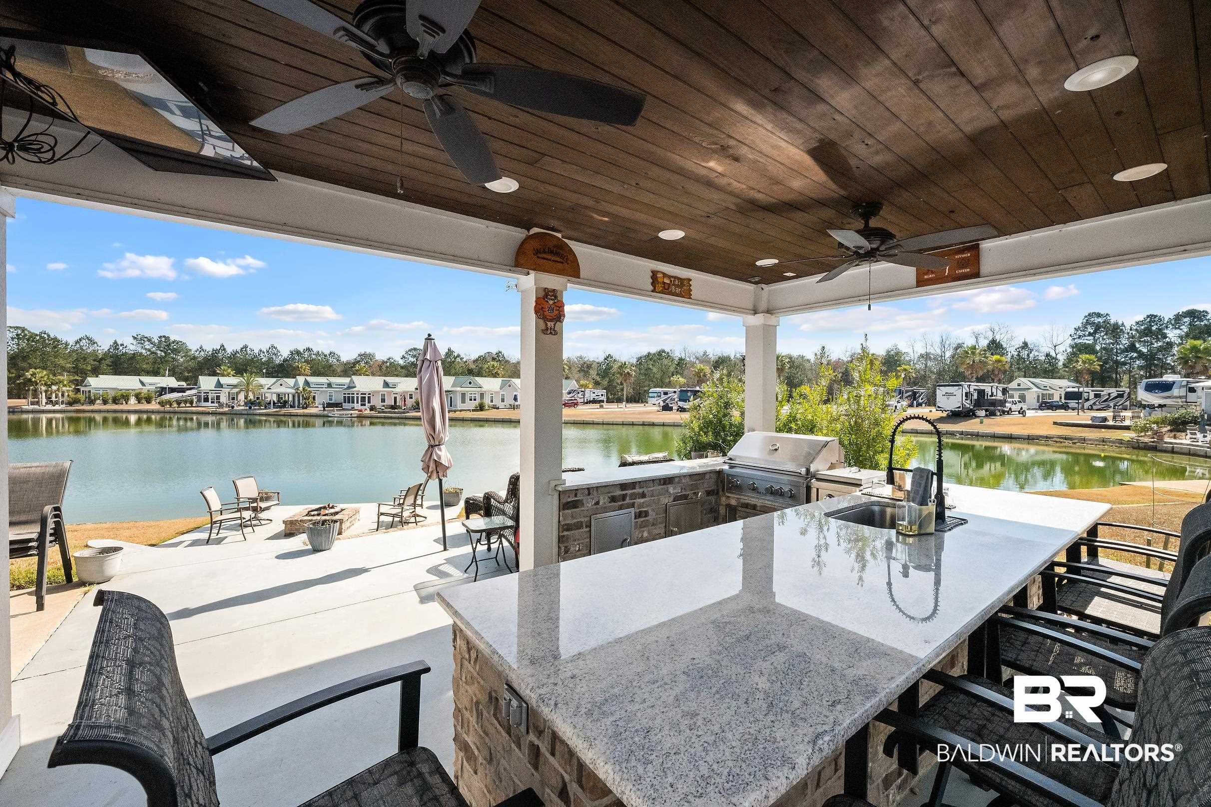 View of patio featuring area for grilling, a ceiling fan, a fire pit, an outdoor bar and dining area, and a water view