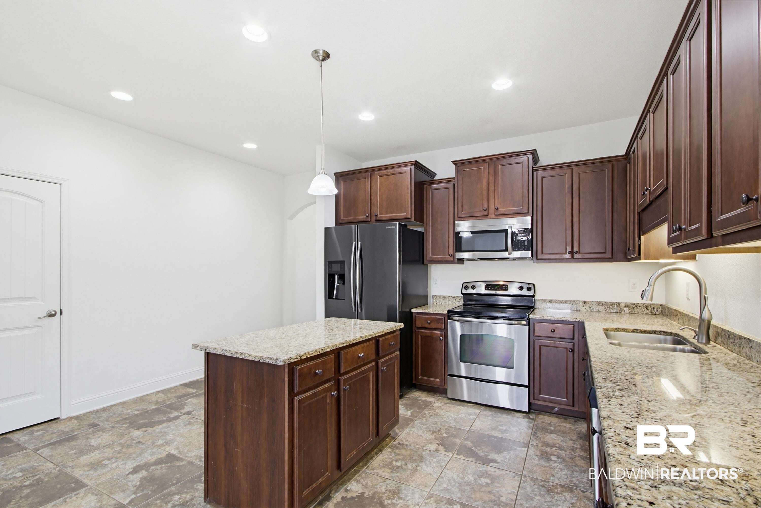 Kitchen featuring a central island with a light-toned countertop, dark wood cabinetry, stainless steel appliances, recessed ceiling lighting, and tile flooring