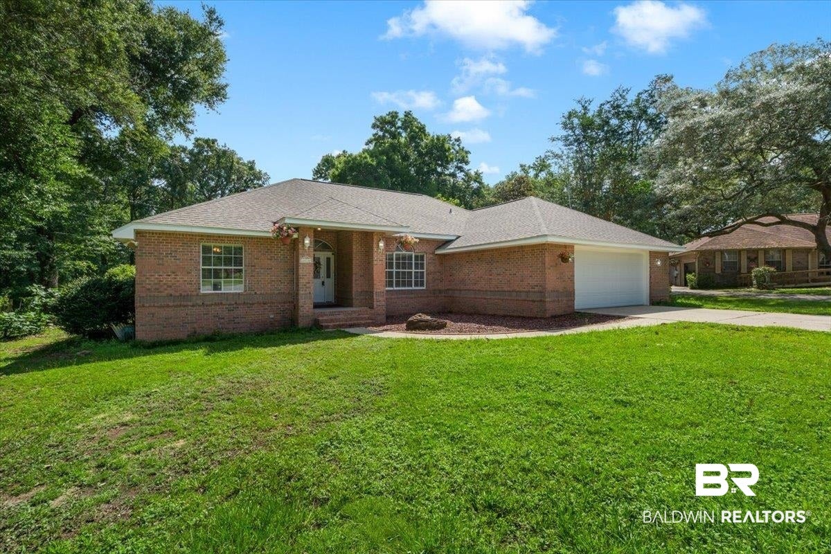 Brick exterior featuring a two-car garage, mature trees, and a spacious front lawn