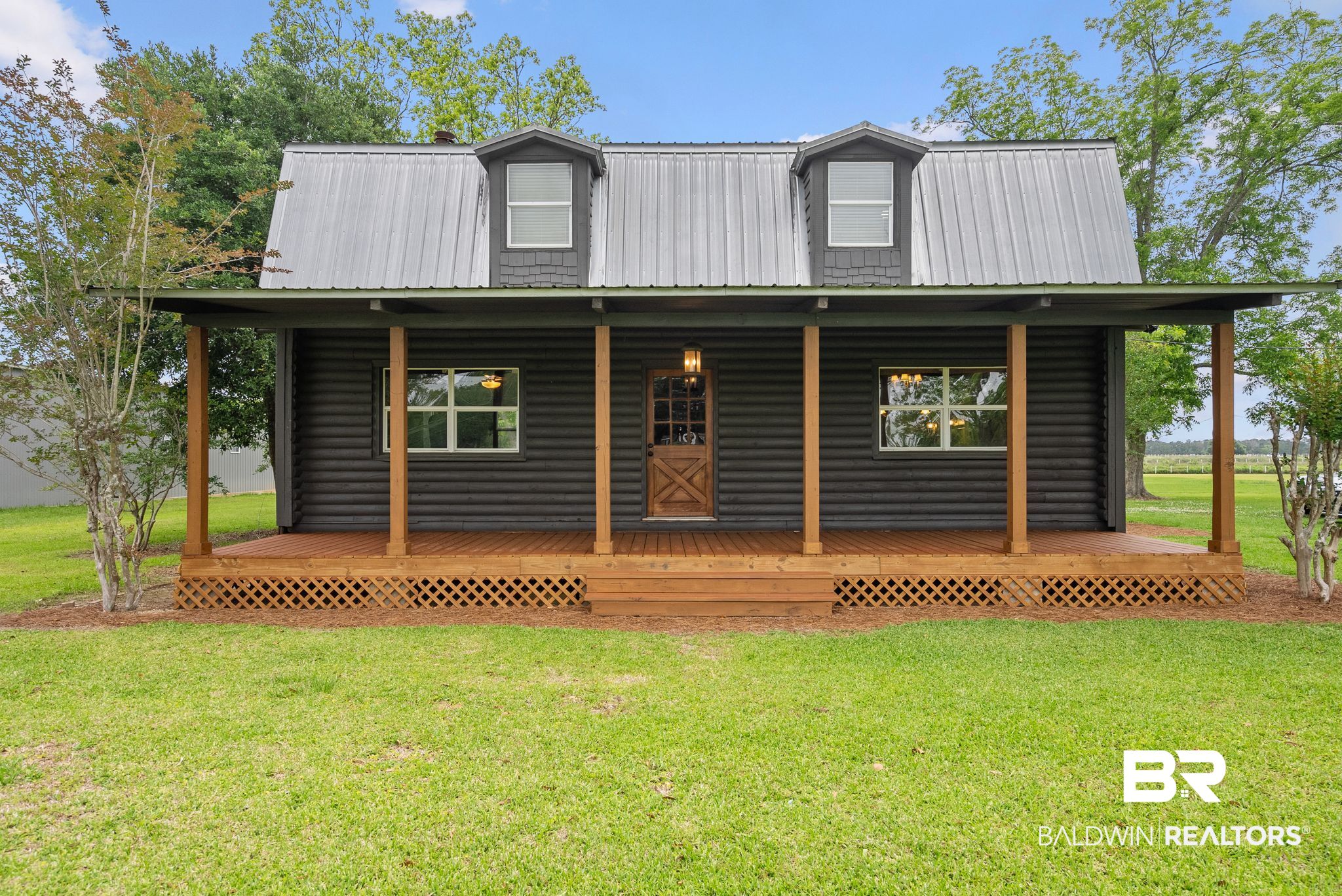 Charming black log cabin exterior with a full-width covered porch, exposed wood support beams, and a metal roof