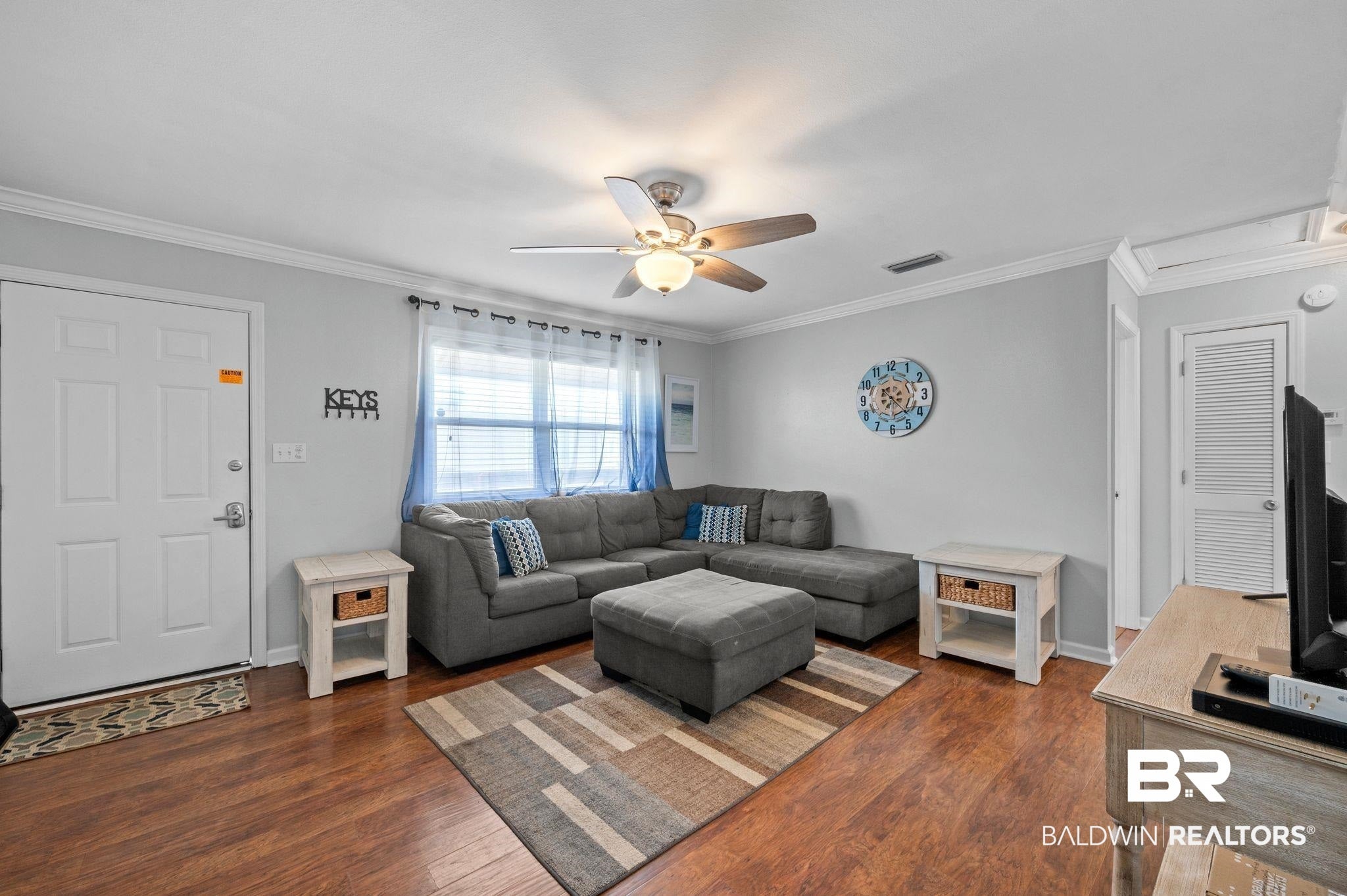 Living area with dark wood-style floors, crown molding, a ceiling fan, and visible vents