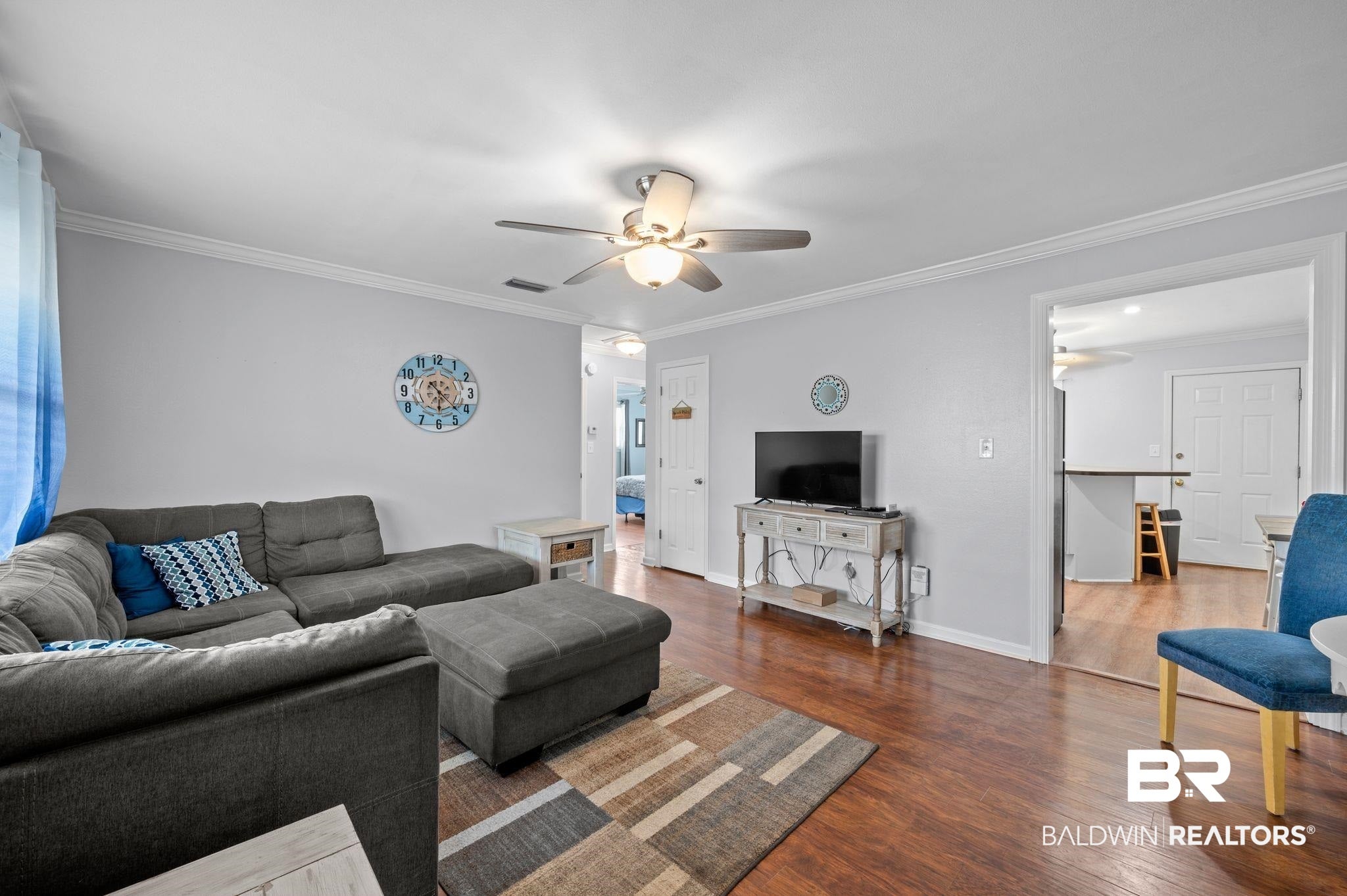 Living room with visible vents, baseboards, a ceiling fan, crown molding, and wood finished floors