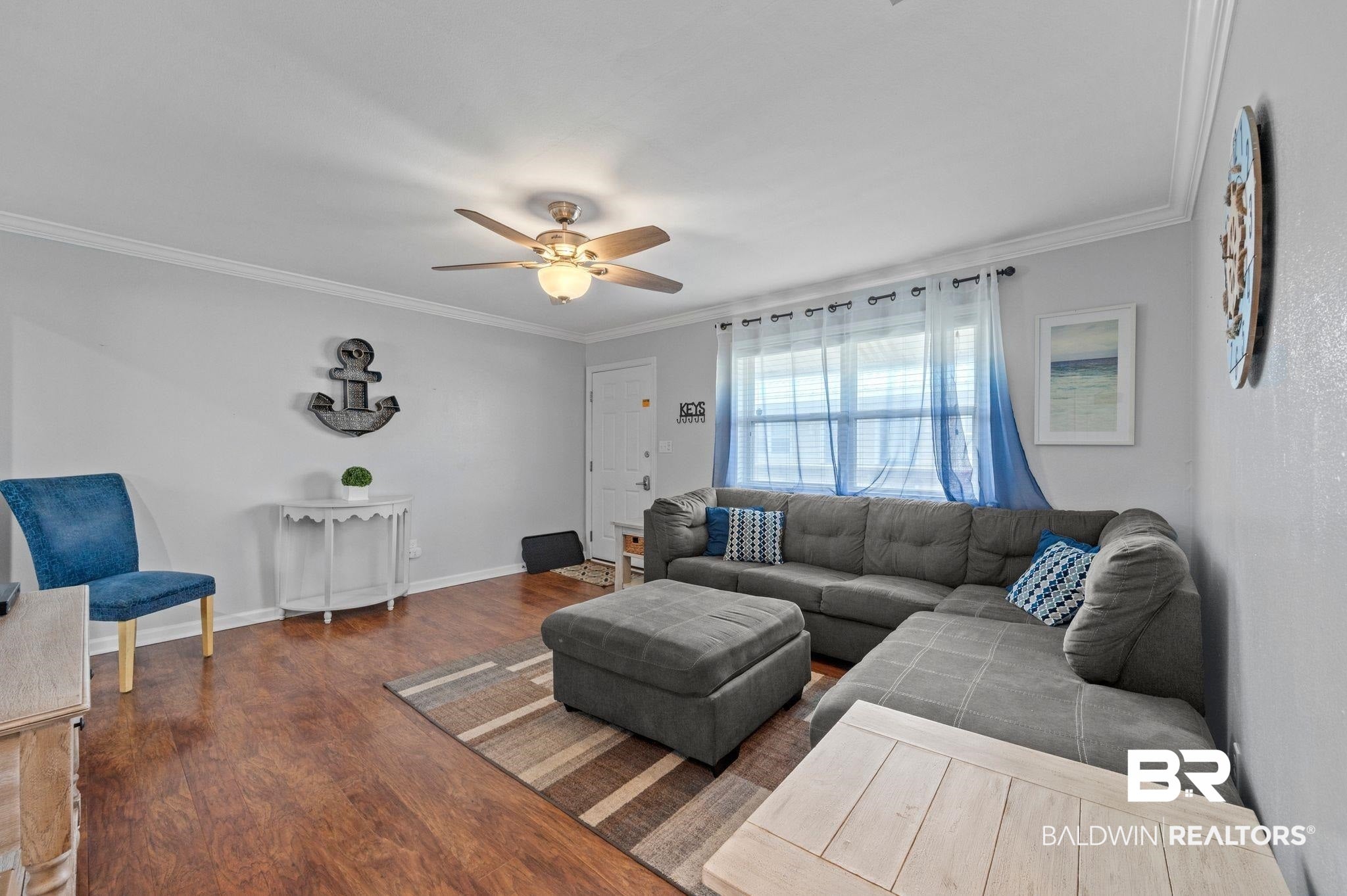 Living room with baseboards, a ceiling fan, crown molding, and wood finished floors