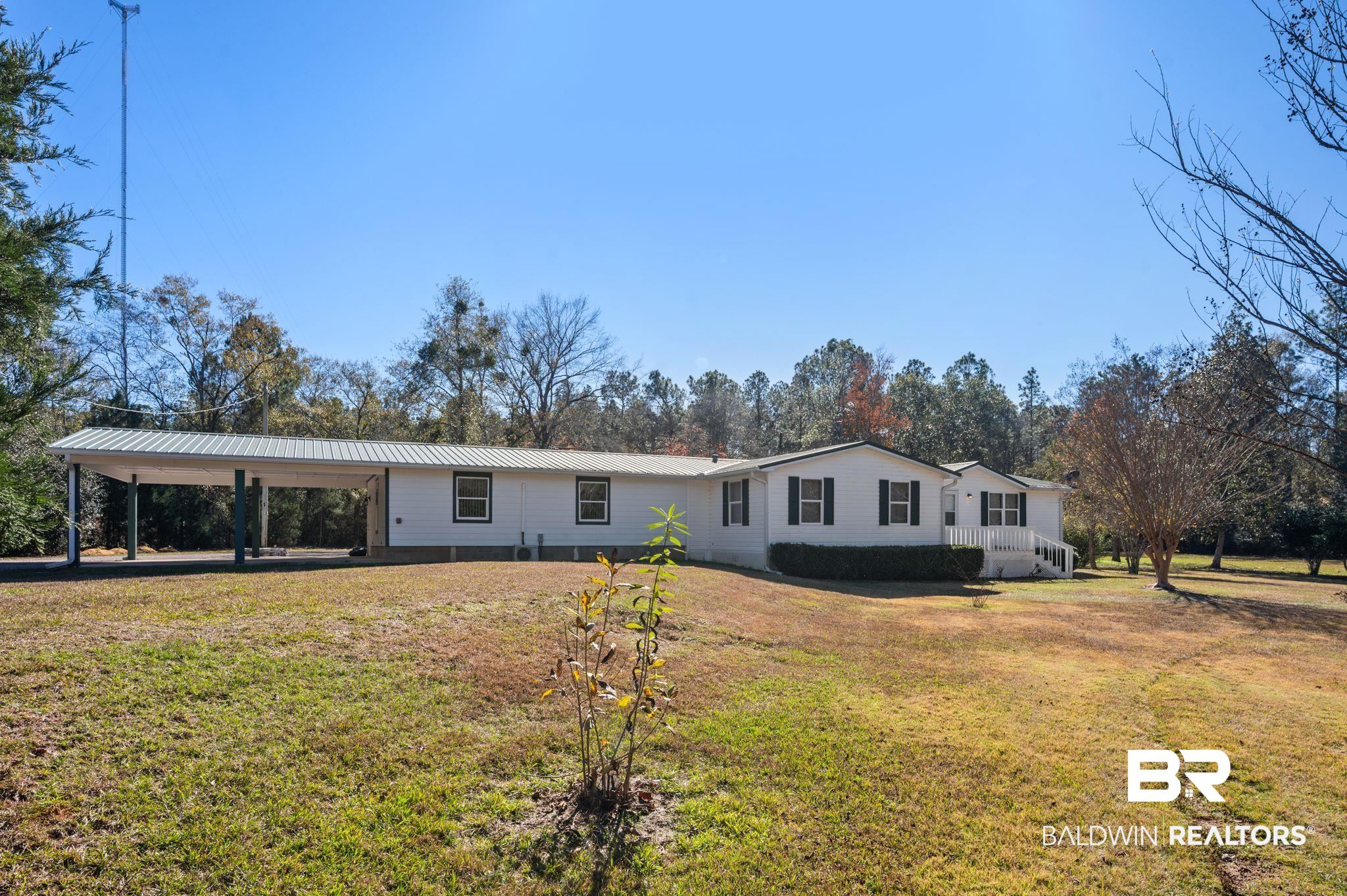 View of front facade featuring a front lawn, a metal roof, a carport, and view of scattered trees