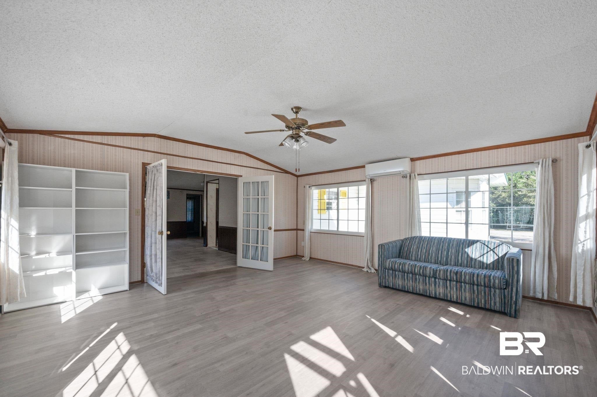 Living area with lofted ceiling, a textured ceiling, ornamental molding, ceiling fan, and wood finished floors