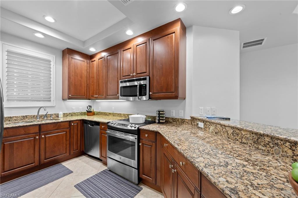 Modern kitchen with dark wood cabinets, stainless steel appliances, granite countertops, and tile flooring, featuring a bright and inviting layout ideal for entertaining in the Vista Pointe residence.