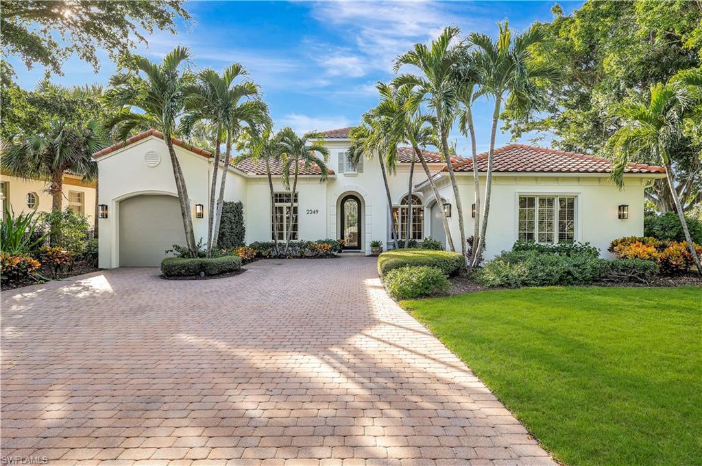 Elegant luxury home exterior at 2249 Miramonte CT in Grey Oaks, featuring a landscaped front yard, palm trees, and a paver driveway, showcasing the upscale lifestyle of Naples, Florida real estate.