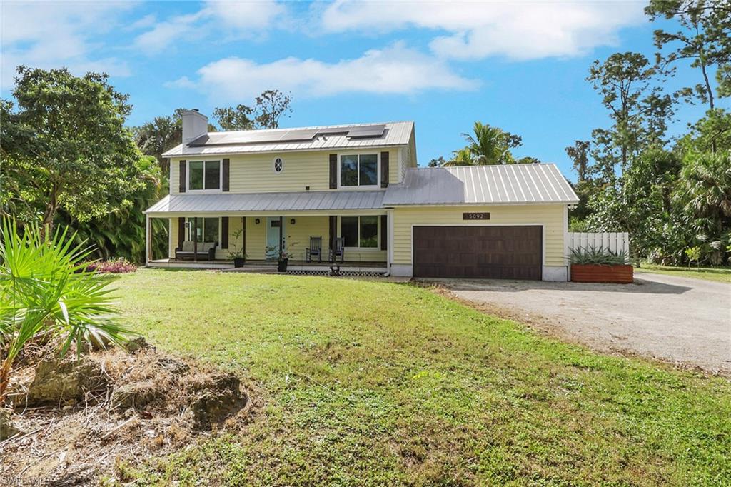 4-bedroom farmhouse-style home in Logan Woods, Naples, featuring a spacious front porch, metal roof, and lush landscaping, highlighting the property's private estate setting.