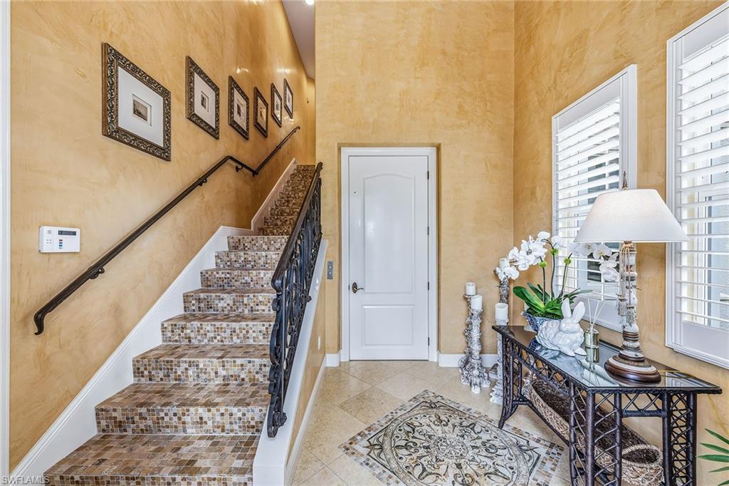 Elegant entryway of a luxury condominium in Avellino Isles, featuring a staircase with decorative tile, framed artwork on the walls, a stylish console table with decorative plants and a lamp, and a warm, inviting ambiance.
