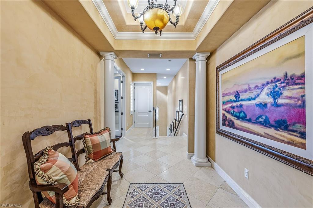 Elegant entryway of a three-bedroom condominium in Avellino Isles, featuring decorative artwork, tiled flooring, and a cozy seating area with pillows, highlighting luxury living in Naples, Florida.