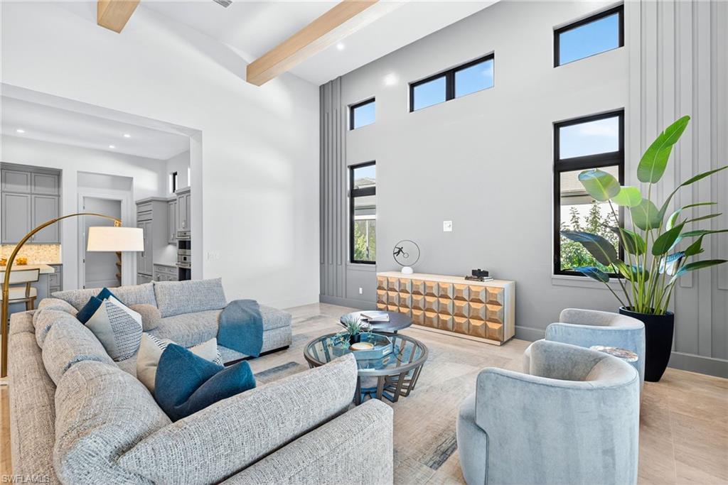 Modern living room in new construction home, featuring plush gray sectional sofa with decorative pillows, stylish accent chairs, large windows for natural light, contemporary light fixtures, and a decorative console table, highlighting elegant design and spacious layout ideal for entertaining.