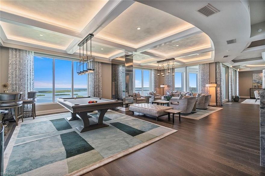 This iconic residence crowns the 23rd floor of Seaglass at Bonita Bay, where two units have been masterfully combined into a singular, 6,000-plus-square-foot designer showcase with expansive outdoor living. Every inch reflects opulence and visionary artistry by the renowned Collins & DuPont team, earning its feature in Florida Design Magazine for elevated, livable design. Framed by uninterrupted Gulf and Bay views through soaring floor-to-ceiling windows, the condominium offers a sensation of floating above it all like a bird in flight. Western-facing balconies offer retractable screens and hurricane shutters, creating year-round comfort and protection while delivering front-row seats to the Gulf’s ever-changing canvas and majestic sunsets. The great room flows effortlessly into multiple living and entertainment spaces: a piano nook, lounge area, pool table zone and dining—all anchored by a gourmet kitchen that would make any chef swoon. Rich wood tones contrast against crisp quartz countertops, a sprawling center island, and cabinetry that feels more like bespoke furniture. Even the view from the sink is striking. In the dining area, a custom wet bar elevates entertaining, while LED-lit radius ceilings add sculptural drama throughout. Even the powder room and laundry room shimmer with designer touches. The primary suite offers a serene, Gulf-facing retreat with a spa-style bath, oversized glass-enclosed shower, double vanities, and a boutique-style walk-in closet with multiple quartz islands. Two en-suite guest bedrooms on the east wing offer luxury and privacy for family and visitors. Two separate office spaces provide flexibility for remote work, hobbies, or can be easily converted into additional guest suites. A dedicated den offers an immersive cinematic experience. A private, air conditioned two-car garage and two additional parking spaces complete this rare offering. Your masterpiece in the sky awaits.