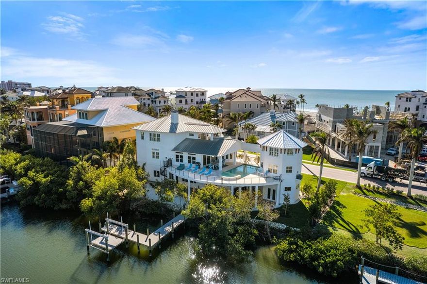 Beautifully renovated estate with breathtaking wide bay views in North Naples’ premier community of “Barefoot Beach”. A true boater and beach lover’s paradise, this home features deeded beach access only a 2-minute walk away and direct Gulf-access from your private dock with a brand-new boat lift. Every detail of this residence has been thoughtfully upgraded, including a new roof, elegant travertine and wood flooring, hurricane-impact windows and doors, and soaring coffered ceilings. Spanning 5,000 sq ft under air, this home offers 4 spacious bedrooms + a den, 4.5 bathrooms, a separate guest villa, dual laundry rooms, a private elevator and a ground-floor flex space. The outdoor space is truly an entertainer’s dream, offering sweeping bay views, an elevated pool and spa, an outdoor shower, and ample lounging areas—both covered and open. The oversized chef’s kitchen is a true masterpiece, featuring sleek quartz countertops, beautiful mahogany wood cabinetry, an induction cooktop, a breakfast bar, and an inviting eat-in area. The luxurious primary suite is a serene retreat, offering direct access to a private balcony overlooking the water—ideal for enjoying your morning coffee. A spacious office/sitting room, a fireplace, a wet bar with a built-in fridge, and a spa-like bathroom with dual vanities, a separate jetted tub, and a large frameless glass shower complete this tranquil sanctuary. The separate guest suite is perfect for hosting, offering 2 bedrooms, 2 bathrooms, and its own laundry facilities for added privacy. This is the epitome of coastal living. Optional membership to the exclusive "Club at Barefoot" provides access to tennis, two restaurants, beachside food and beverage service, and more. Conveniently located near fine dining, RSW Airport, Mercato, and Waterside Shops, and just 15 miles from the renowned Fifth Avenue in Naples, this home is a true gem in the heart of Barefoot Beach.