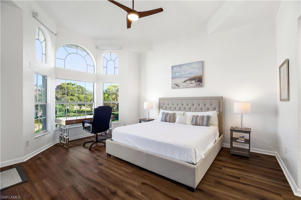 Bright bedroom with vaulted ceilings and large windows overlooking lush landscaping, featuring a queen bed, modern desk, and stylish decor in a condominium at 6030 Chardonnay, The Vineyards.