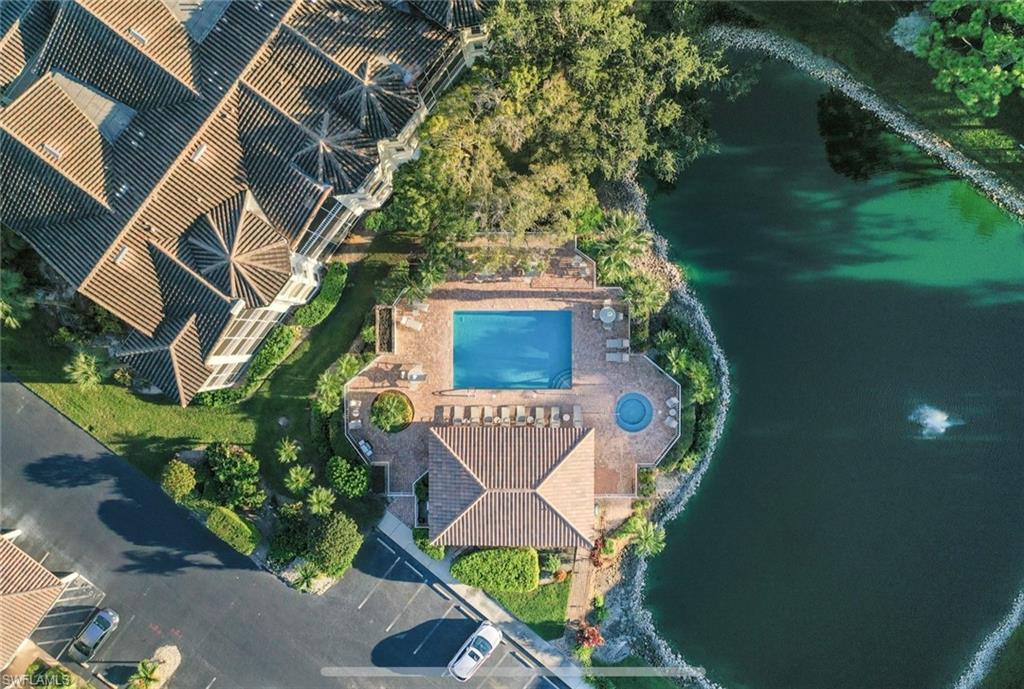 Aerial view of a condominium complex in Naples, Florida, featuring a resort-style pool surrounded by tropical landscaping and a tranquil pond, highlighting the lifestyle amenities of The Vineyards community.