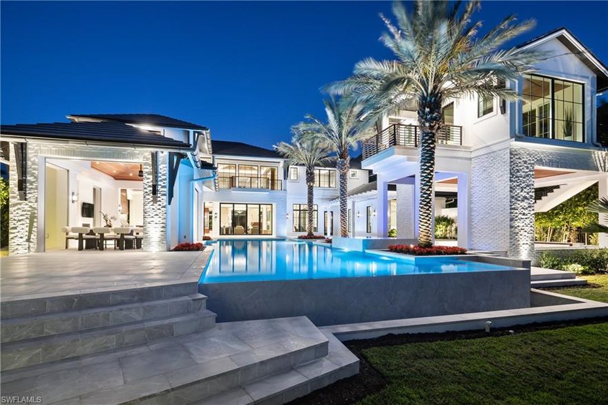 NOW COMPLETE!  Commanding a rare, western lakefront view in Old Naples, this new construction estate redefines scale, craftsmanship, and architectural clarity. Encompassing over 9,400 square feet of interior living space, the home was conceived as a private resort - where every element supports both the grand and granular aspects of daily living. Twin infinity-edge reflecting pools frame the entrance, opening into a dramatic two-story great room with precision millwork, architectural symmetry, and a sculptural floating staircase. Adjacent, a formal dining room is anchored by a custom, glass-enclosed wine wall integrated into bespoke cabinetry. The kitchen, defined by a curved steel-and-glass partition, includes Wolf/Sub-Zero appliances, dual Miele coffee stations, and a concealed butler’s pantry equipped for large-scale entertaining. Subtle finishes and architectural restraint elevate the overall atmosphere. The first-floor primary suite is entirely self-contained, featuring a private study, two oversized dressing rooms, a discreet laundry center, and a marble-clad bath with indoor/outdoor showers. Upstairs, five additional bedroom suites are complemented by a media lounge and a concealed club room with full bar and humidor. Outdoor architecture is equally refined. A 60-foot negative-edge pool extends across the rear elevation, interrupted by a series of stepping-stones that lead to a sunken firepit lounge surrounded by water. An elevated spa, covered loggia, and summer kitchen complete the space. Above it all, a detached fitness pavilion with breath-taking wide lake vistas, introducing a compelling architectural counterpoint. Additional features include 13x Toto Neorest toilets, three laundry stations, a commercial-grade sheet ironer, full-home generator, elevator, and a five-car split garage designed for collectors. A comprehensive smart home system governs all functions discreetly. Realized by New England based developer EMB Custom Homes, and executed by MHK Architecture, Lotus Construction, and Freestyle Interiors, this fully furnished residence is a singular opportunity in the Naples luxury market.