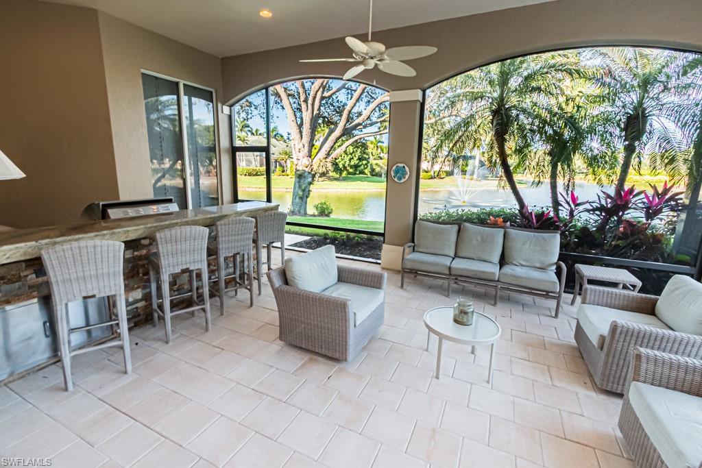 Lakeside outdoor living area featuring a bar with seating, elegant furnishings, and views of lush landscaping and a fountain, highlighting the luxury of the Marsh Links community in Naples, FL.