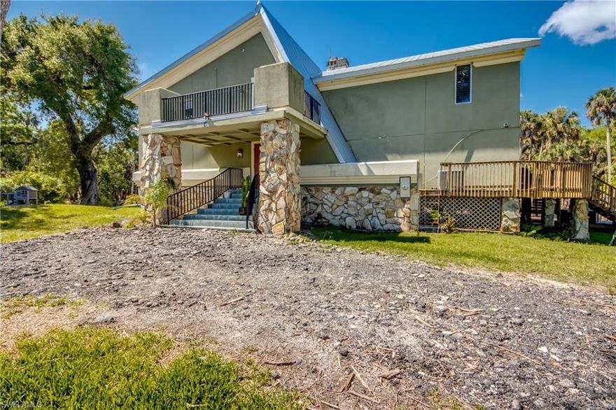 Estate-style riverfront home on 3.28 acres in Buckingham with over 500 feet of frontage on the Orange River and a 3 year old 1,500± sq ft dock. The elevated A-frame residence offers 3,668 sq ft of living area, built on a poured concrete foundation with concrete pilings and steel framing for exceptional durability. Foam insulation under the stucco and three zoned central A/C systems (including one dedicated to the primary suite) help keep the home comfortable and energy-efficient. Whole home Reverse osmosis with 500 gallon tank just installed comes with a 5 year warranty. The main level features an 8x8 mudroom, a full guest bath with large walk-in shower, and an infrared 3-person EMF sauna. The great room showcases a soaring 26-foot ceiling, matching 26-foot river-stone fireplace, and a dramatic Brazilian marble slab accenting one of the structural A-frame beams. The kitchen offers approximately 24 feet of counter space, two lazy Susans, a clay farm sink, cooktop, double convection oven with steam and Wi-Fi probe functions, and a 4x8 walk-in pantry. Recently installed impact-resistant sliding doors provide natural light and added storm protection, a valuable feature in Florida’s hurricane-prone climate.A separate downstairs living area functions as a game room with wet bar and French doors to the wraparound deck. Upstairs are two generous guest bedrooms with Jack-and-Jill bath, attic access for extra storage, and a loft with built-in desk and private deck overlooking the property. The primary suite offers tongue-and-groove ceilings, a 22-foot closet, and a spa-like bath with oversized walk-in shower, seamless glass, dual sinks, and quartz counters.Multiple outbuildings create unmatched flexibility: two main garages (one with workshop, loft, and steel framing), a middle building with roughly 1,000 sq ft of insulated space with drop-in A/C and half bath ideal for a home business or flex use, plus a rear building with built-in shelving, lean-to storage, and back deck. This one-of-a-kind property combines acreage, waterfront, and extensive storage/workspace—perfect for those seeking an estate home, hobby compound, or live/work setup.