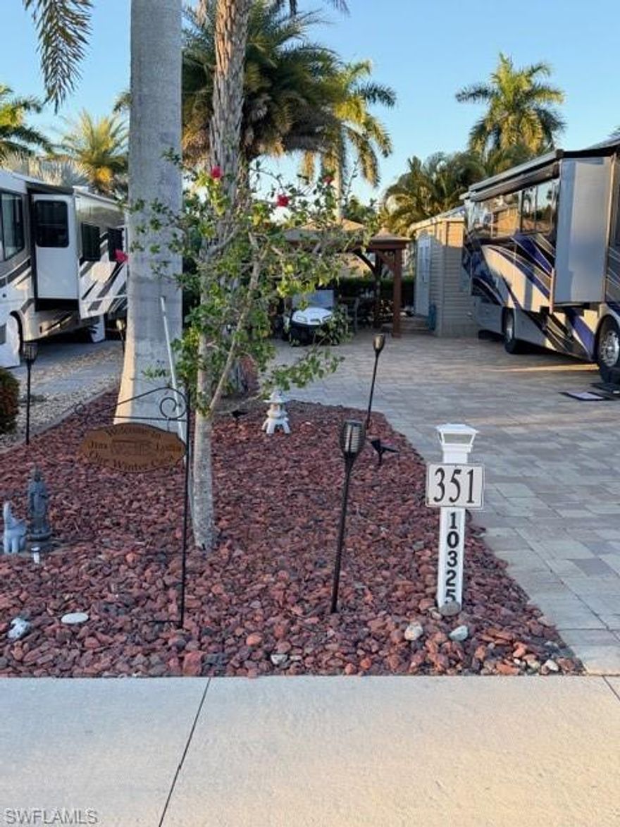 Back into this amazing lot which offers a view of Sunrise Lake across the street.  The lot is a 100% paver lot with nice neutral colors in the pavers.  Enjoy the landscaping with a variety of plants including Sylvester Palms, Mini Date Palms, Areca  Palms and colored lava rocks surrounding the plants.  These plants have a full irrigation system both above and below ground. You can stay shaded or protected from the rain in the 12 x 14 Yardesty rear gazebo.  The lot is only 12 lots from the ballroom, the clubhouse, the pool and the activity center.  If you have dogs you’re allowed two on this lot and it is only a short walk around the corner to the dog park.  On this lot is also a Amazon 10 x 12‘ finished  shed and includes a full size Maytag washer and dryer, a large walk-in shower, a toilet and a vanity with an on demand Rheem hot water heater.  There is a privacy sliding door that separates your main area and has extra storage space above the bathroom as well as extra shelving. The shed is cooled by a window air conditioner.  This is a very well maintained property.  Be sure to call for a private tour.