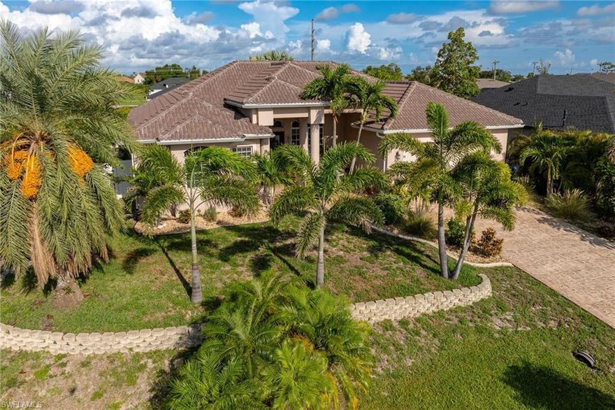 One-of-a-kind custom built pool home located on a spacious corner lot with lush tropical landscaping, mature palms, blooming shrubs, custom concrete curbing and a manicured lawn. This property offers excellent privacy with no through traffic while still being conveniently close to shopping, restaurants and main roadways. The home has been exceptionally well maintained and is truly move-in ready, featuring a brand new $60,000 tile roof, 2021 A/C system, newer smart hot water heater, and gutters all around the home. Leading to the home you’ll find a decorative concrete driveway, elegant double door entry, and as you enter the home your met with soaring volume ceilings and an open layout with both a formal living room and a family room that includes a built-in entertainment center. The kitchen is designed for entertaining with tall cabinetry, plant shelves and plenty of counter space. Each bedroom has its own dedicated bathroom, offering comfort and privacy for family and guests. The primary suite is bright and inviting with a tray ceiling, private slider to the pool, and a luxurious bathroom offering dual sinks, a jetted tub, oversized shower and two walk-in closets. 90-degree disappearing sliders open to seamlessly connect the indoor and outdoor living areas, leading to the expansive screened lanai with a sparkling pool featuring a waterfall, pool heater, covered seating area and a custom outdoor kitchen with built-in grill for outdoor cooking and a sink. The yard is fully fenced for privacy, and best of all this home is not in a flood zone! Don't miss out on a truly one-of-a-kind SW Cape Coral Pool Home!