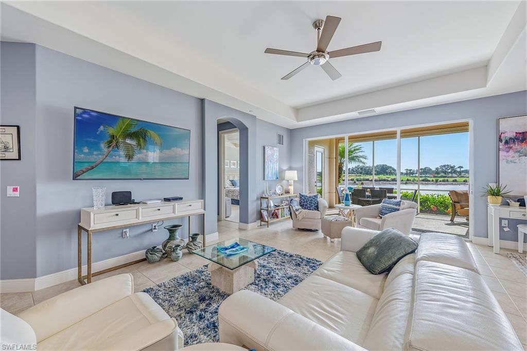 Luxurious living room in Avellino Isles condominium, featuring modern decor, large windows with water and golf course views, and comfortable seating, showcasing a spacious layout ideal for relaxation and entertaining.