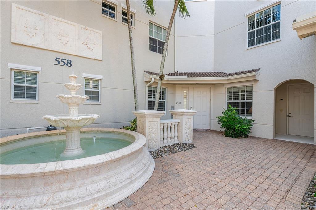 Condominium entrance at 558 Avellino Isles, featuring a decorative fountain, paver walkway, and tropical landscaping, highlighting luxurious living in Naples, Florida.