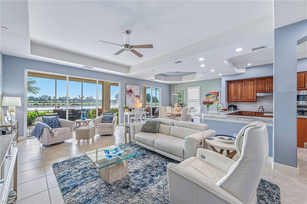 Luxurious living room in Avellino Isles condominium, featuring modern furnishings, large windows with water and golf course views, and an open layout connecting to the kitchen, highlighting a renovated space ideal for entertaining.