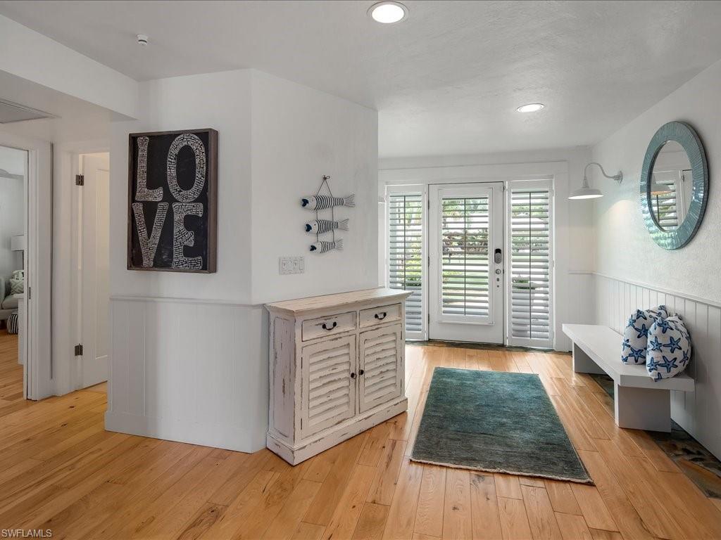 Welcoming entryway of a modern home featuring a 'LOVE' wall art, wooden console table, and decorative pillows, with natural light streaming through plantation shutters and a view of the outdoor space.