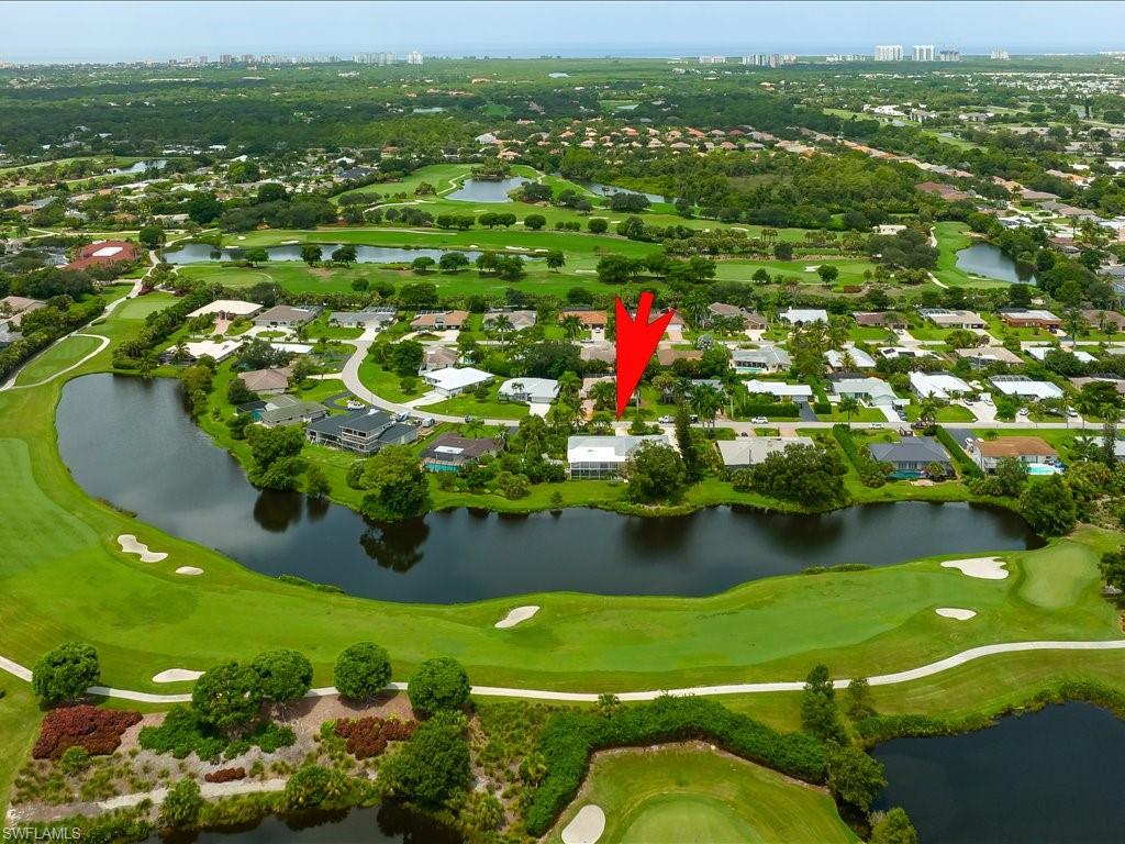 Aerial view of a residential neighborhood in Palm River Estates, Naples, Florida, highlighting a property with lake and golf course views, marked with an arrow, showcasing lush greenery and well-maintained homes.