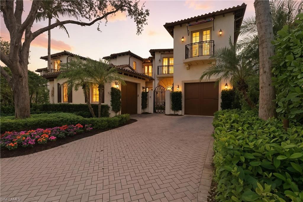 Elegant two-story residence in Grey Oaks, featuring lush landscaping, paver driveway, and warm evening lighting illuminating the home&rsquo;s architectural details.