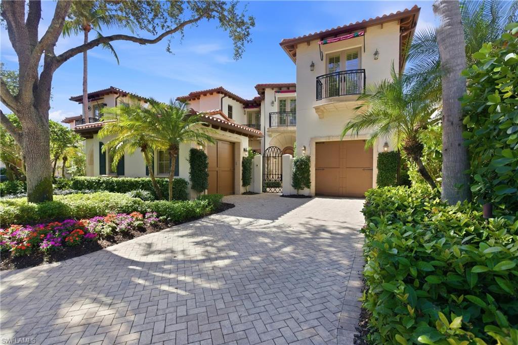 Elegant two-story residence in Grey Oaks, Naples, featuring lush landscaping, paver driveway, and palm trees, showcasing luxury living with proximity to golf course views.