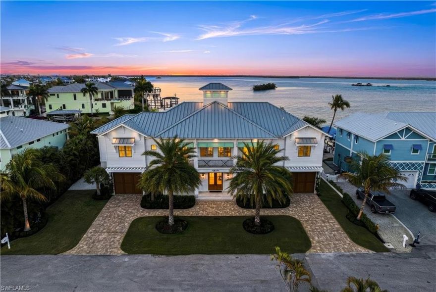 2022-built bayfront masterpiece with deeded beach access and an elevated pool and spa, perfectly positioned on the peaceful south end of Estero Island. Located on an extra-wide homesite with a double-wide driveway, this exceptional coastal retreat offers 120 feet of waterfrontage and sweeping, unobstructed bay views. A true beach and boater’s paradise, the property includes dual boat lifts—a covered 16,000 lb lift and an additional 10,000 lb lift—and is located less than a quarter mile from the sugar-sand shores of Fort Myers Beach. This home features a Galvalume metal roof, hurricane-impact windows and doors, electric storm shutters, and electric sliders that seamlessly blend indoor and outdoor living. The elevated saltwater pool and spa can be heated by gas or electric and showcases a tanning ledge and water features, while the fully equipped summer kitchen with swinging chairs and fireplace creates the ultimate entertainer’s setting. The outdoor space also offers a spacious yard, covered lanai, and expansive dock ideal for fishing and waterfront relaxation. Inside, approximately 3,481 square feet of thoughtfully designed living space includes 3 bedrooms plus an office (or optional 4th bedroom), 4.5 bathrooms, ground-floor flex space, elevator, and garage space for 10+ vehicles. The coastal contemporary interior is meticulously crafted with beautiful oak flooring, soaring ceilings with custom details, a grand wood staircase, and abundant natural light throughout. The chef’s kitchen is beautifully appointed with illuminated Cristallo countertops and backsplash, white and ocean-blue cabinetry, high-end appliances, and a butler’s pantry. The primary suite serves as a private retreat with direct access to the pool deck, stunning water views, a large custom closet, and a spa-like bath featuring Cristallo counters, dual vanities, a soaking tub, and an oversized glass-enclosed shower with multiple showerheads. Additional highlights include an automatic whole-home generator, two tankless water heaters, electric interior shades, Lutron lighting system, and surround sound system. Ideally located on a quiet stretch of South Estero Island near fantastic dining, Lovers Key and Bonita Beach, and just minutes from Times Square and the vibrant energy of Fort Myers Beach, this home represents the pinnacle of waterfront living.
