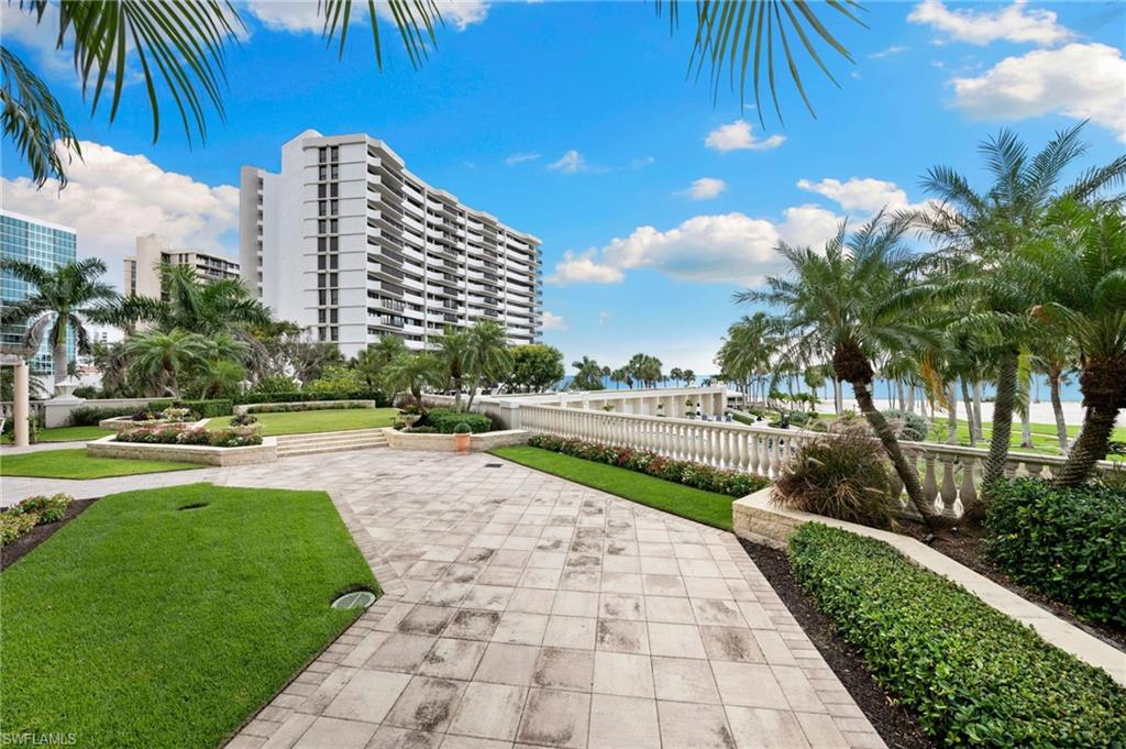 Beachfront garden residence at The Brittany in Venetian Village, Naples Florida, featuring lush landscaping, paved pathways, and views of the Gulf, showcasing a luxurious outdoor living space ideal for entertaining.
