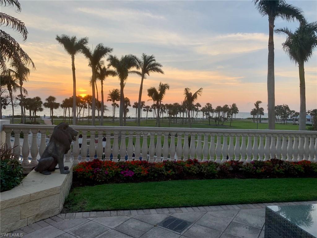 Beachfront sunset view from The Brittany residence, featuring palm trees, landscaped gardens, and a lion statue in the foreground, highlighting luxurious outdoor living in Naples, Florida.