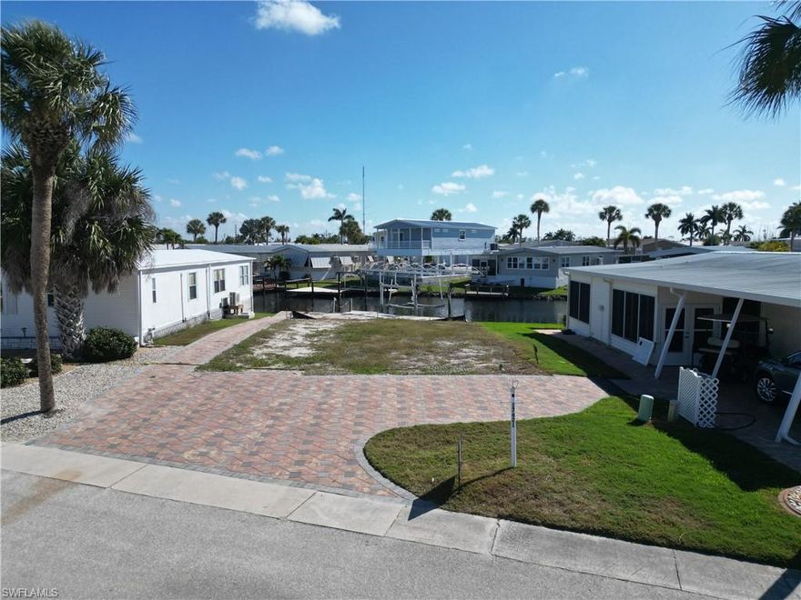Bayside Estates has essentially two half’s, split down the middle by Stevens Blvd. There is the retention pond side and the saltwater side. Both have their benefits. This lot is located on the retention pond side so there is always plenty of water in the canals. Once on the other side of the boat lift, the waterway to Hurricane Bay, Hell Peckney Bay, the Gulf of Mexico and beyond is completely unobstructed. Go shopping and pick out the manufactured home of your liking and have it delivered to this lovely lot and begin partaking in the benefits of this highly desirable community. As you can see, this lot has thousands of dollars in custom paver work, making your new home shine brightly. When looking to buy a vacant lot in Bayside Estates, you might consider a lot that has a seawall that is in good condition and a lot that already has a boat dock and boat lift included. This is one such lot. The boat lift has the aluminum structure in place for a boat cover. Bayside Estates is the best kept secret of Fort Myers Beach. This incredibly active and friendly 55+ community is the crown jewel on the gulf coast. Bayside estates is only 2.5 miles to the beach and is accessible by either car or boat--right from either your driveway or private boat dock. A very popular activity is riding your electric bicycles to the beach for the day and visit the world-famous Jimmy Buffett’s Margaritaville. Just don't step on a pop-top!!. Nearly all of the major retail vendors are within a very short driving distance for ultimate convenience. For those who don’t know a lot about Bayside Estates, it is a very fun place to call home---some would even say it’s a mature person’s playground. Whether you want to play pickleball, tennis or bocce ball or hang out at the community pool, or simply cruise the hood in your golf cart, there is always something going on around here. People are friendly and you will be warmly welcomed.
