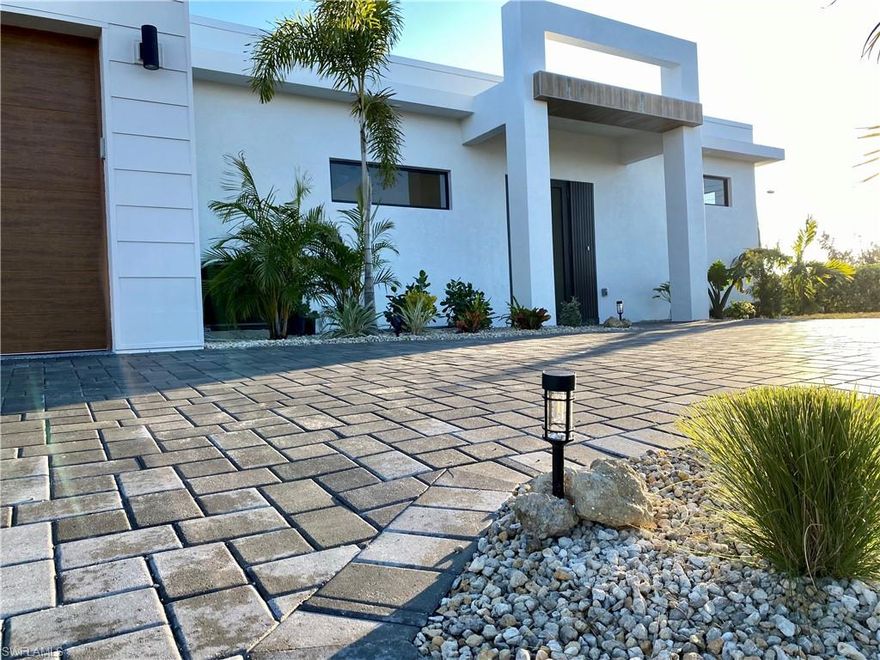 Tired of the same old basic builder house?  Welcome to your new modern luxury Miami style home with all the essential upgrades at an affordable price.   NO FLOOD ZONE in one of Cape Coral's best neighborhoods, which means no costly flood insurance required.  Enjoy your WATER VIEW in the backyard on a freshwater canal across from all beautiful new construction homes!  Exterior boasts plush landscaping with several palm trees and a colorful shrub assortment surrounded in landscaping stones all around the home.  Paver driveway with extra parking area in front to showcase your luxury vehicles with wood texture impact garage door leading into your polyaspartic epoxy garage floor.  Stucco exterior with upgraded waterproofing and self cleaning paint that will stay looking clean for years to come.  14 foot exterior entry with wood like tile on the ceiling facade leading you to the 8 foot front door with privacy glass where inside you will be greeted with the stunning waterfall island with upgraded Panda Calacatta quartz design on the countertops and backsplashes in the kitchen, bathrooms and laundry room.  11 foot ceilings in the great room, kitchen and dining rooms and 9 feet everywhere else. 12 foot triple sliding door leading to your covered patio and another sliding door off of the kitchen for open concept entertaining bringing the inside to the outdoors.   Ample sized L-shape kitchen with practical layout has two tone 40" high cabinets with many drawers and storage, pull out trash and full height pantry.  Nice sized island that will fit 4 stools. Warm LED lighting on all upper cabinets for chill mode with modern light fixtures to compliment the modern design.  Half bathroom included with easy access in the main wing of the home.  Laundry room has a sink and dedicated folding area.  Master bathroom has LED lit mirrors and LED double sink vanity, with separate make-up vanity area for her, next to the open concept walk-in closet with ventilated wood shelving for all wardrobe and storage needs.  Recessed and oversized shower with shiny marble veined porcelain tiles with rain shower and linear drain for easy cleaning.  Recessed ceiling lighting throughout.    To name a few upgrades that MOST HOMES DO NOT HAVE:  Certified testing of the entire house with extremely air tight ENERGY EFFICIENT SCORE (lower than 90% of Cape Coral homes) which means LOW ELECTRIC BILLS!  Underground electric service unlike most homes with the dangerous power line hanging above your home. The home’s foundation sits at the highest elevation in the neighborhood and will never flood.  8 foot height Impact doors and impact windows throughout providing tons of natural sunlight and protection!  Modern flat roof system with multiple waterproofing layers and white UV reflectant coating to reduce heat in the hot summers and keep your home warm and cozy in the winters.  The backyard has a designated 40x20 foot area ready for your underground pool which does NOT require a retaining wall