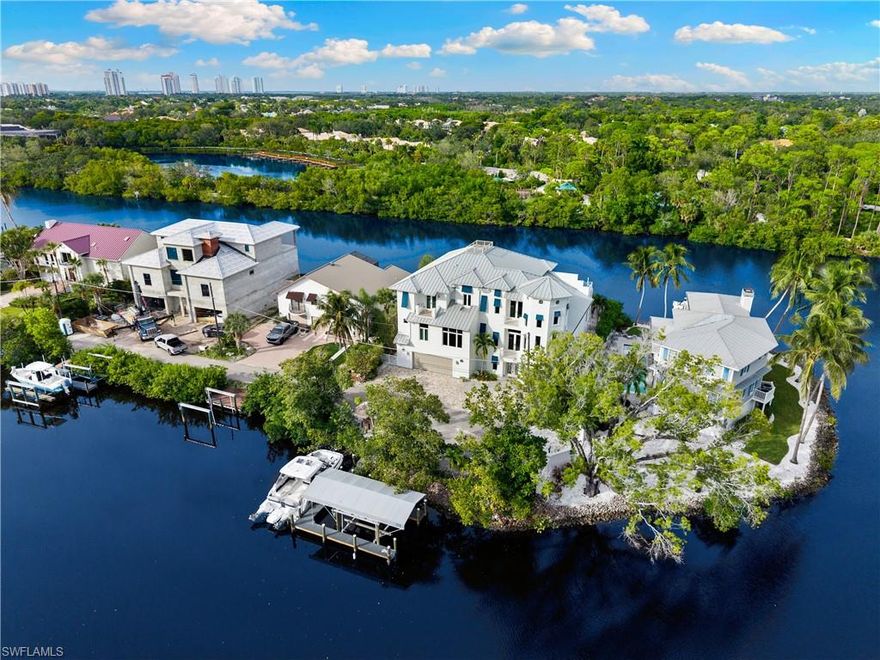 Coastal contemporary riverfront home with beautiful water views from nearly every window. Experience breathtaking long river views with a protected preserve park beyond, offering exceptional privacy. A true beach and boater’s paradise, this property is just a short walk or bike ride to Bonita Beach and Barefoot Beach, and offers Gulf-access with the ideal boating setup including a private dock, covered lift, and tiki hut. Built in 2015 by renowned Potter Homes, this residence was constructed like a fortress with all-concrete construction, hurricane-impact windows and doors, and a metal roof. Fantastic open floor plan with over 5,000 sq ft under air, 5 bedrooms + den, 5.5 baths, and a 4-car garage. The chef’s kitchen boasts dual-toned countertops, white cabinetry, a gas range, and a beautiful stone tile backsplash. Perfect for entertaining, the living room offers beautiful tray ceilings and 10-foot sliders that open to the spacious lanai with electric screens, a fireplace, and a built-in grill, all overlooking the resort-style backyard with a large heated pool, spa, and private beach area. Primary suite is located on the main living floor and offers direct lanai access and a spa-like bath featuring dual vanities, a tub, and a large walk-in shower. Upstairs, enjoy additional bedrooms and living space along with an expansive balcony with panoramic water views. Additional highlights include a private elevator, 22kW generator, newly painted exterior, and ground-level flex space. With no HOA fees or rental restrictions, this property also presents an excellent investment opportunity. Ideally located near top dining and shopping, just minutes from Mercato, The Promenade, Waterside Shops, Coconut Point, 5th Avenue, and the International Airport.