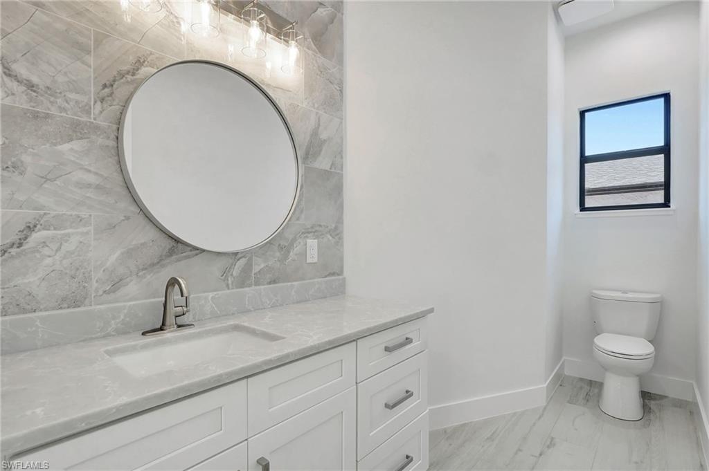 Modern bathroom featuring a round mirror, sleek vanity with gray countertops, stylish faucet, and a window providing natural light, showcasing contemporary design elements in a newly constructed Naples Park home.